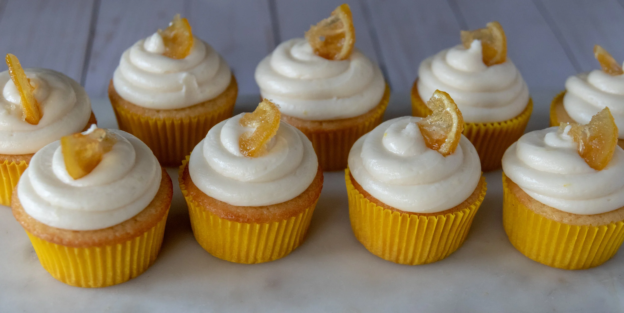 A line of delicious vegan lemon cupcakes with cream cheese frosting garnished with candied lemons.