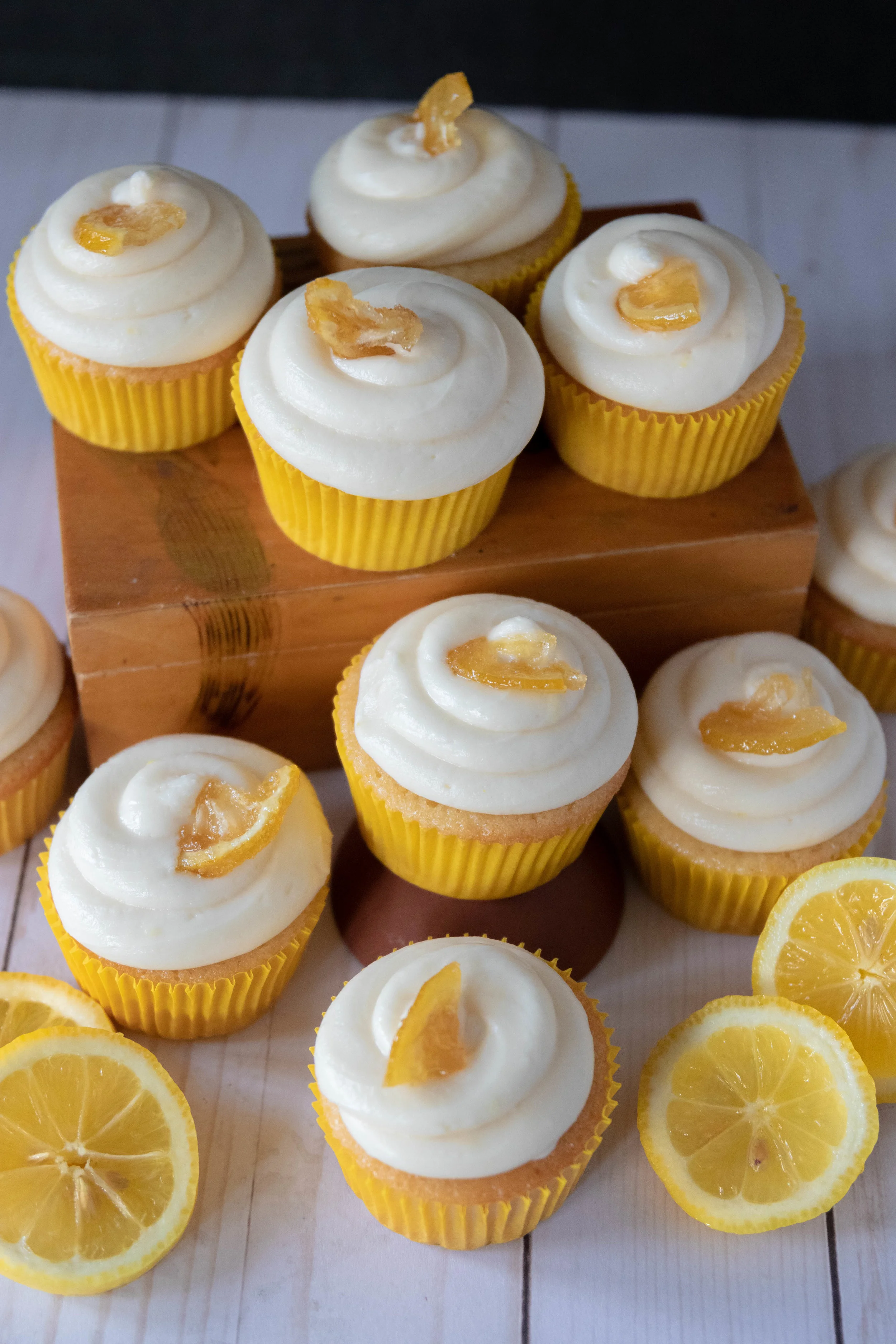 A spread of delicious vegan lemon cupcakes with cream cheese frosting garnished with candied lemons.