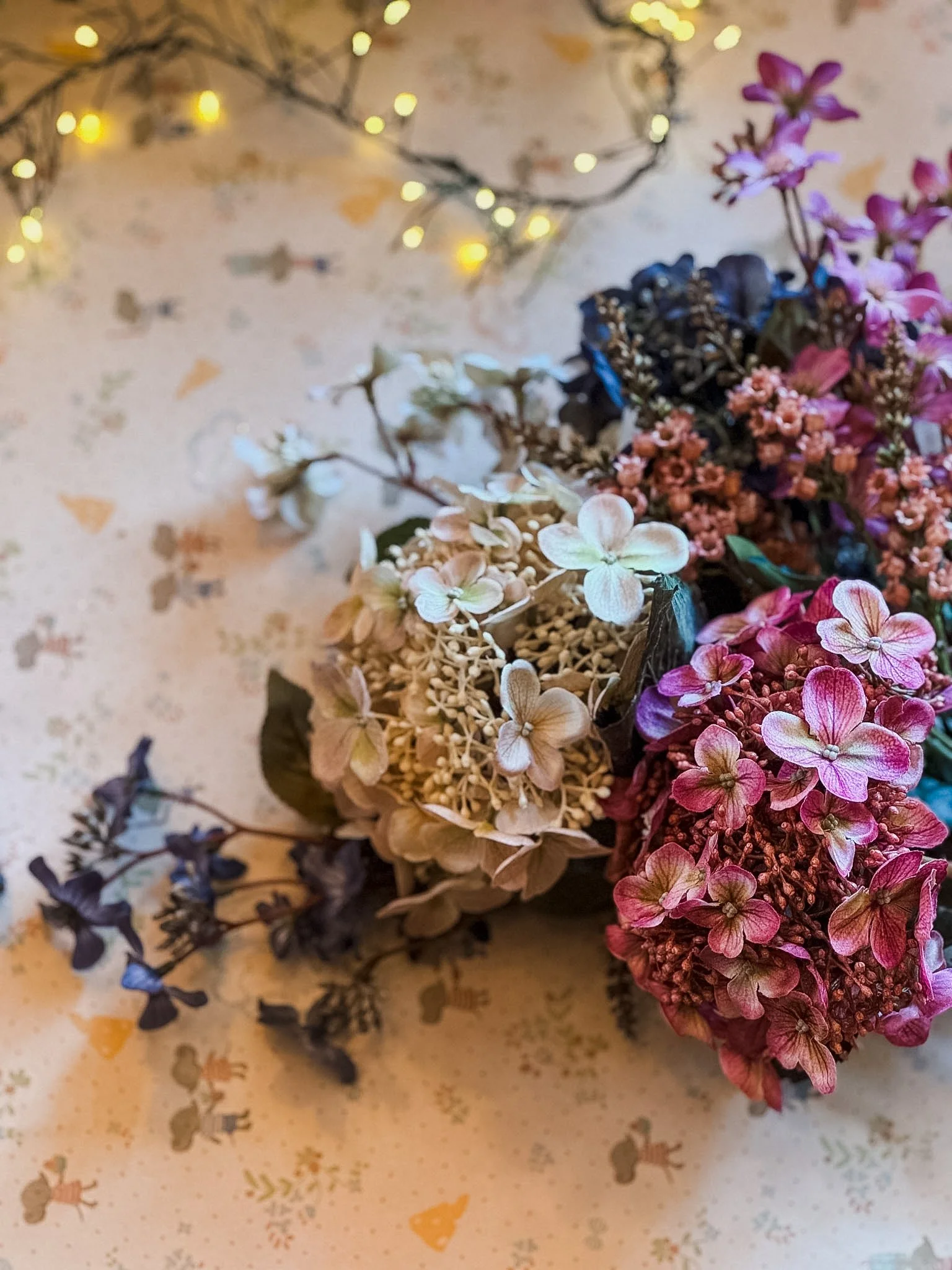Colorful bouquet of dried flowers on a speckled surface with fairy lights in the background.