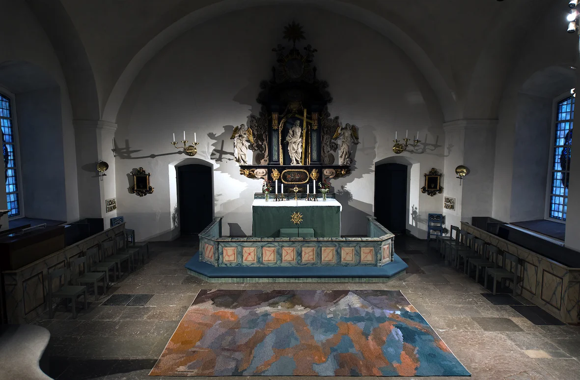 Kormatta Rättviks kyrka 2017 Komposition Alice Lund Textilier/Helena Hernmarck Rölakansteknik, vävd av Malin Svennung Malmén och Emma Moore Rättviks kyrkas kormatta är ett möte mellan en abstrakt akvarell och handvävningens möjligheter. Mattan är tänkt att sätta ett konstnärligt märke från vår tid samtidigt som den ska hålla i många decennier framöver, både formmässigt och kvalitetsmässigt. Kompositionens blå och roströda färgfält är tänkta att korrespondera med marmoreringarna på snickerierna. De mörka, intensiva tonerna återkommer i predikstolen. De mjuka formerna stämmer väl in med resten av kyrkorummets arkitektur och golv. Den abstrakta akvarellen utmanar rölakanteknikens strama uttryck och ett nytt möte skapas i vävstolen. Foton: Pär K Olsson
