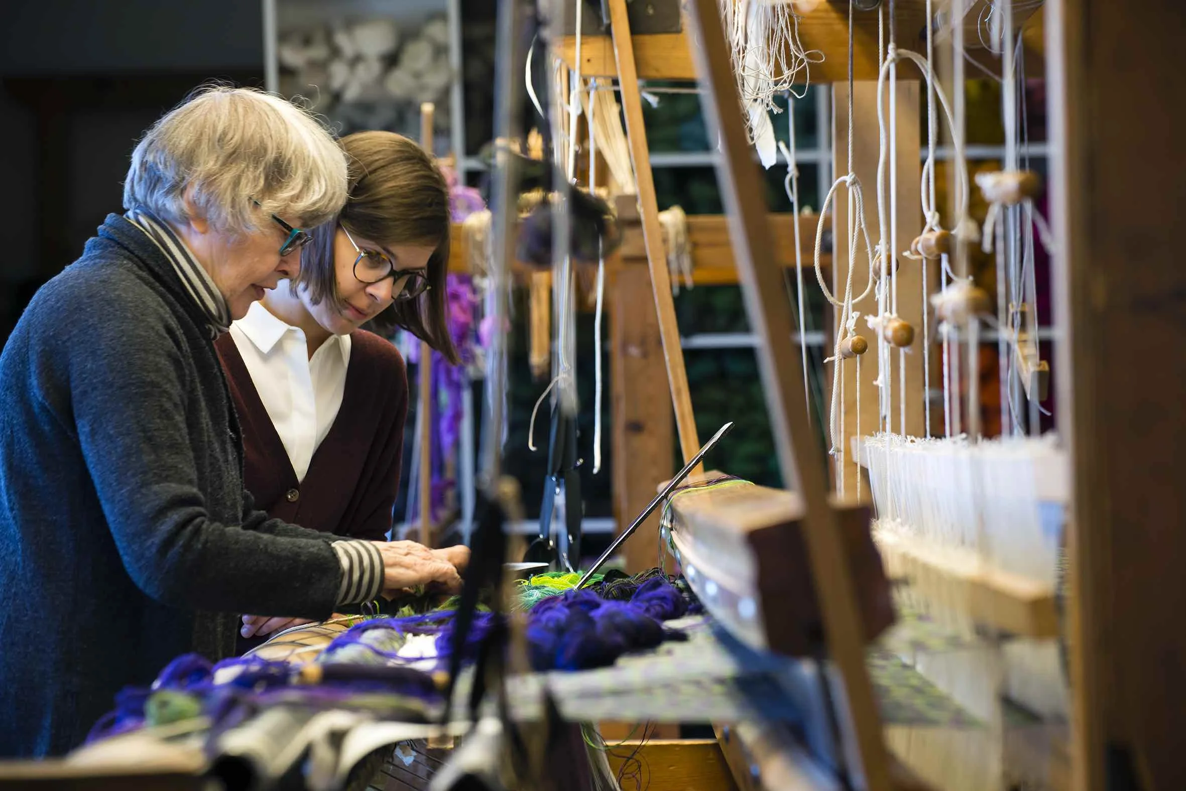 Helena Hernmarck har arbetat med monumental textil konst för offentlig miljö i över femtio år, ofta i samarbete med kända arkitekter. I den fritt experimenterande amerikanska textilkonsten är hon unik genom att hålla fast vid och vidareutveckla sitt svenska textilarv; traditionella vävtekniker och berättande bildvävar. Sedan 1975 har Helena samarbetat med Alice Lund Textilier och ateljén har vävt över 20 stora bildvävnader genom åren. Foto: Helena Hernmarck och Frida Lindberg vid vävstolen på Alice Lund Textiliers ateljé 2017