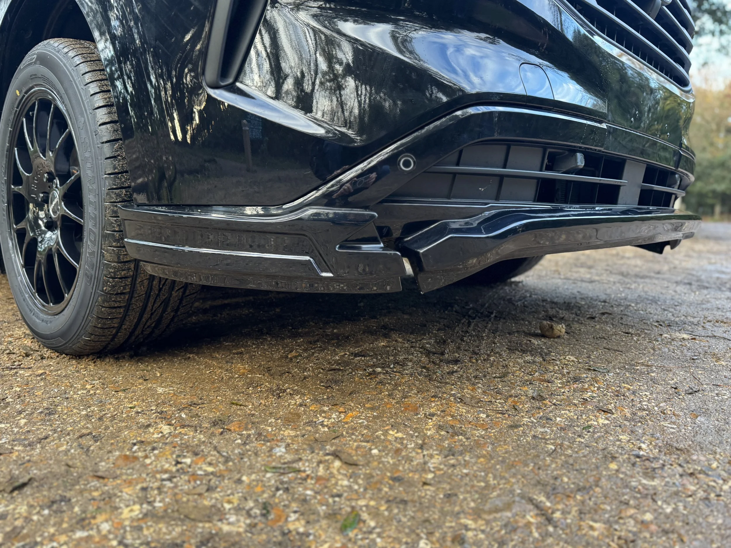 Close-up of the front right side of a black SV Sport Van, showing the tire, wheel, and lower bumper with parking sensors.