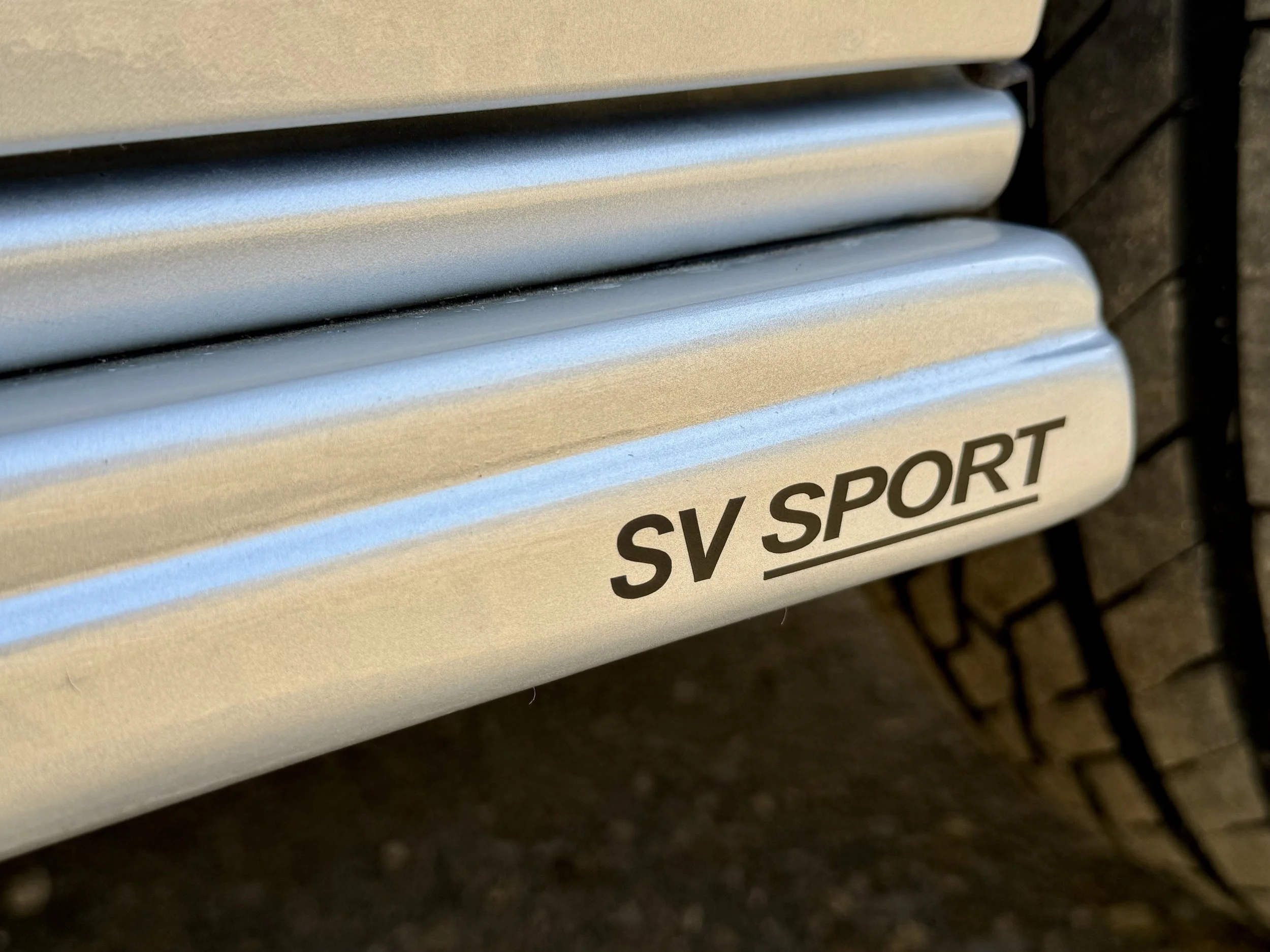 Close-up of a metallic bench with the text "SV SPORT" printed on it, set against a brick wall.