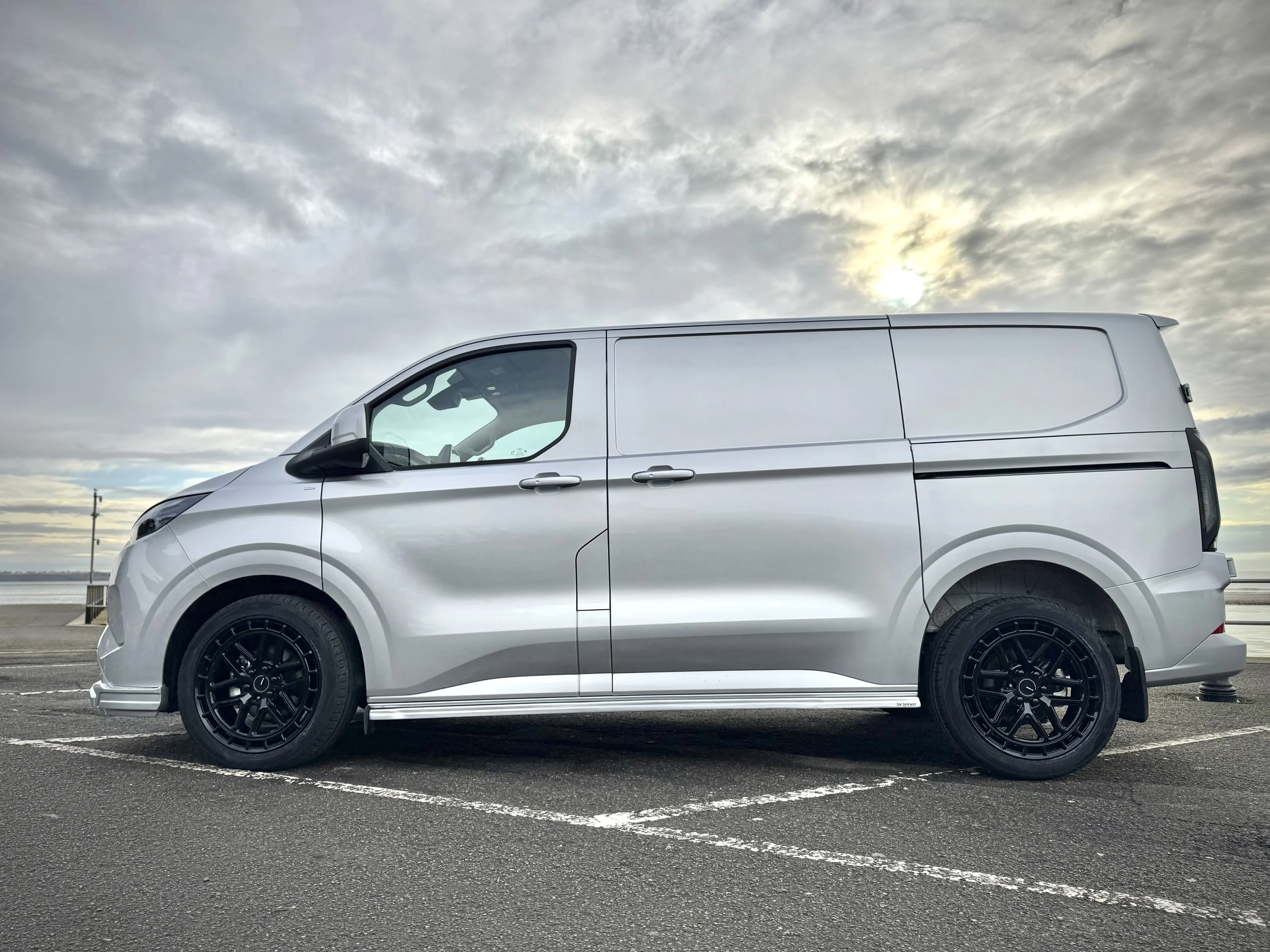 Silver cargo van parked in a parking lot under a cloudy sky during daytime.