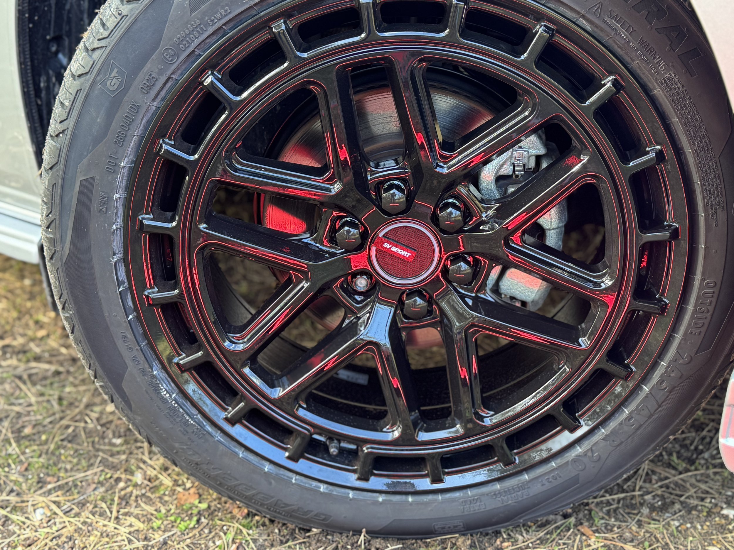 Close-up of a black alloy wheel for a ford transit Custom SV Sport Van  with red accents on a car tire, showing the SV Sport logo in the center.