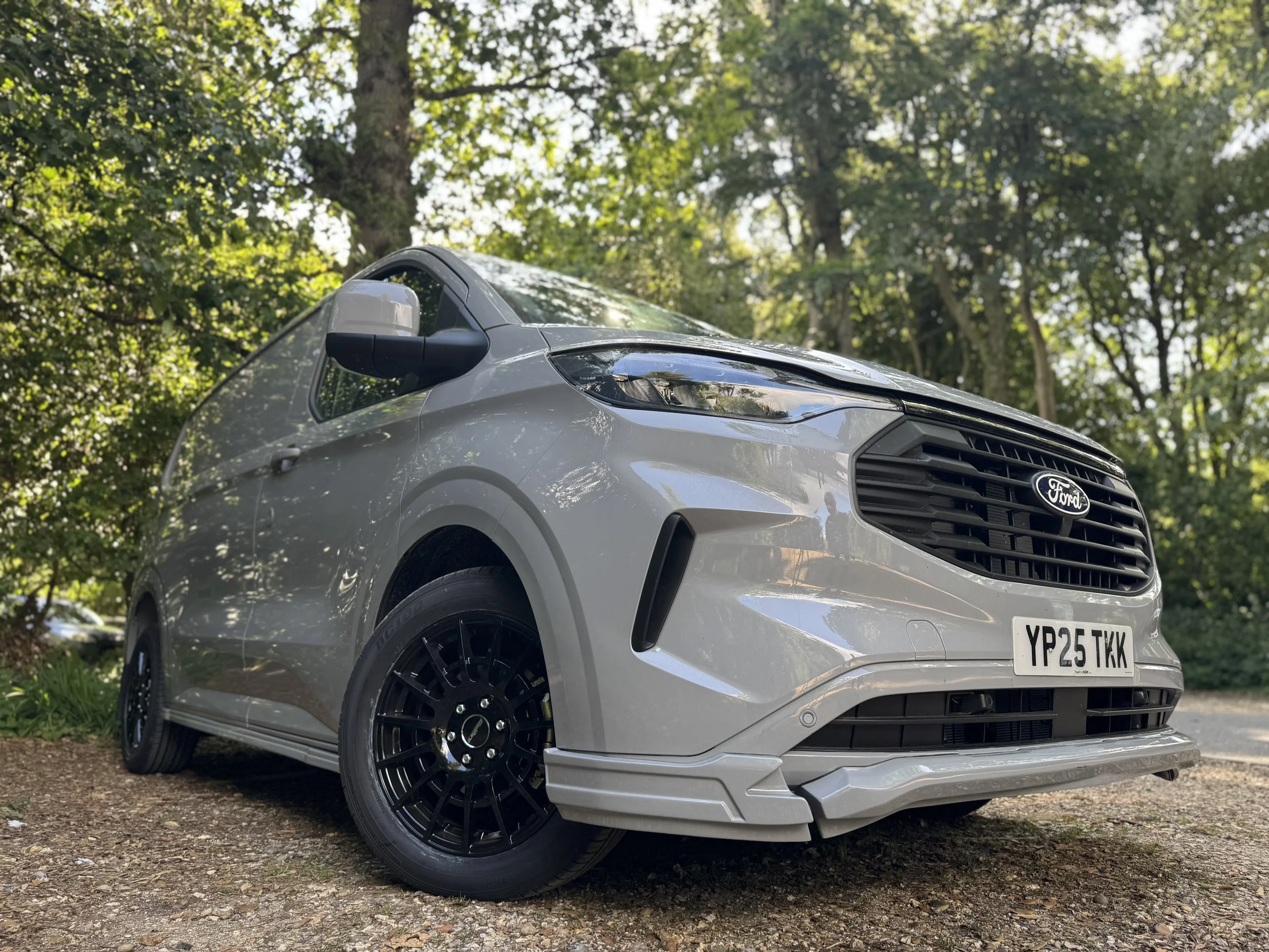 Silver Ford Transit Custom Sport van parked on a dirt path with trees and greenery in the background. the van is fitted with a Body kit from SV Sport 