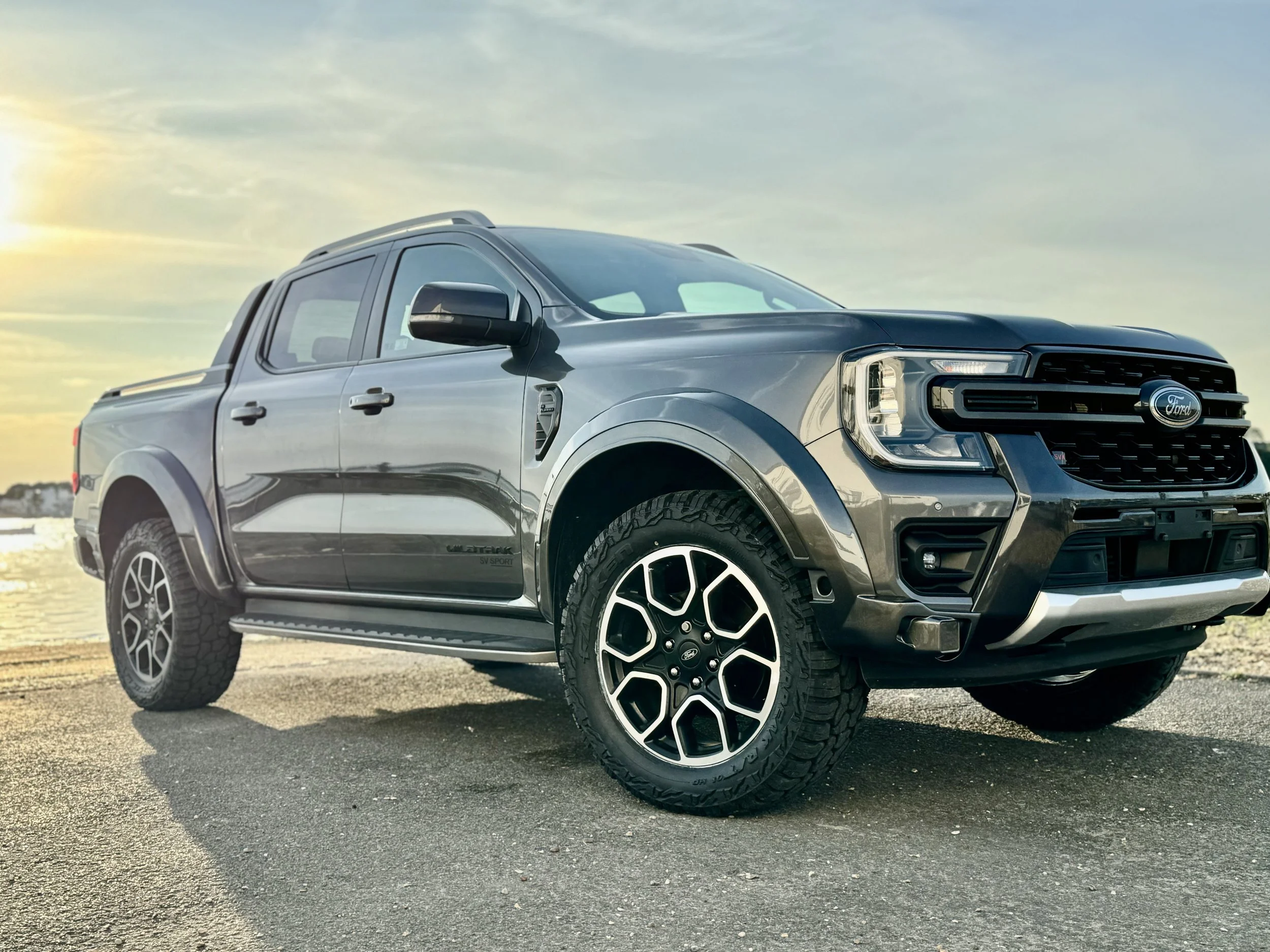 A gray Ford Ranger pickup truck parked near water during sunset. It has an aggressive body kit styling from SV Sport vans 