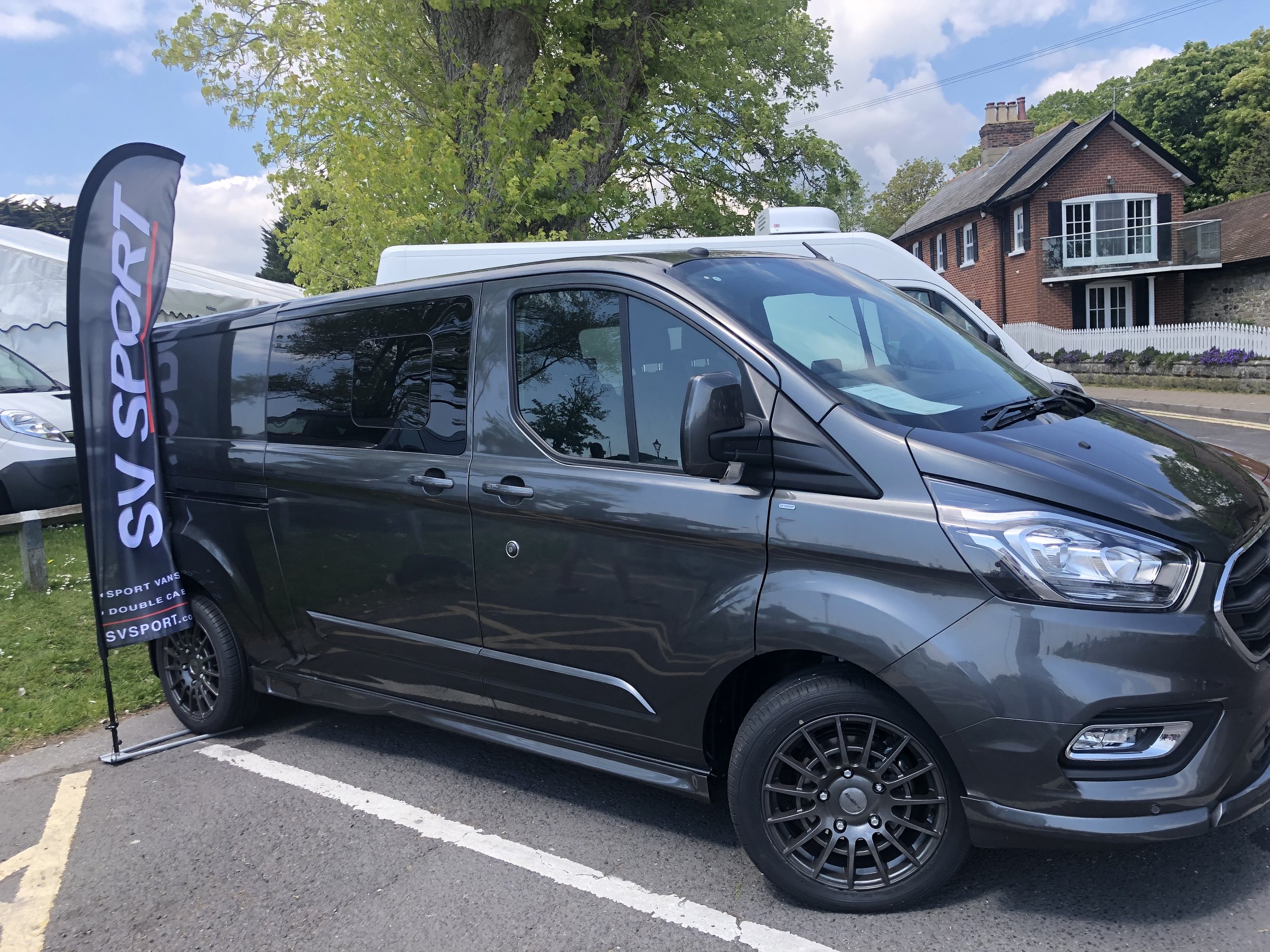 Black Ford Custom Double Can in van with SV SPORT flag next to it, parked in a lot on a sunny day with trees and houses in the background.