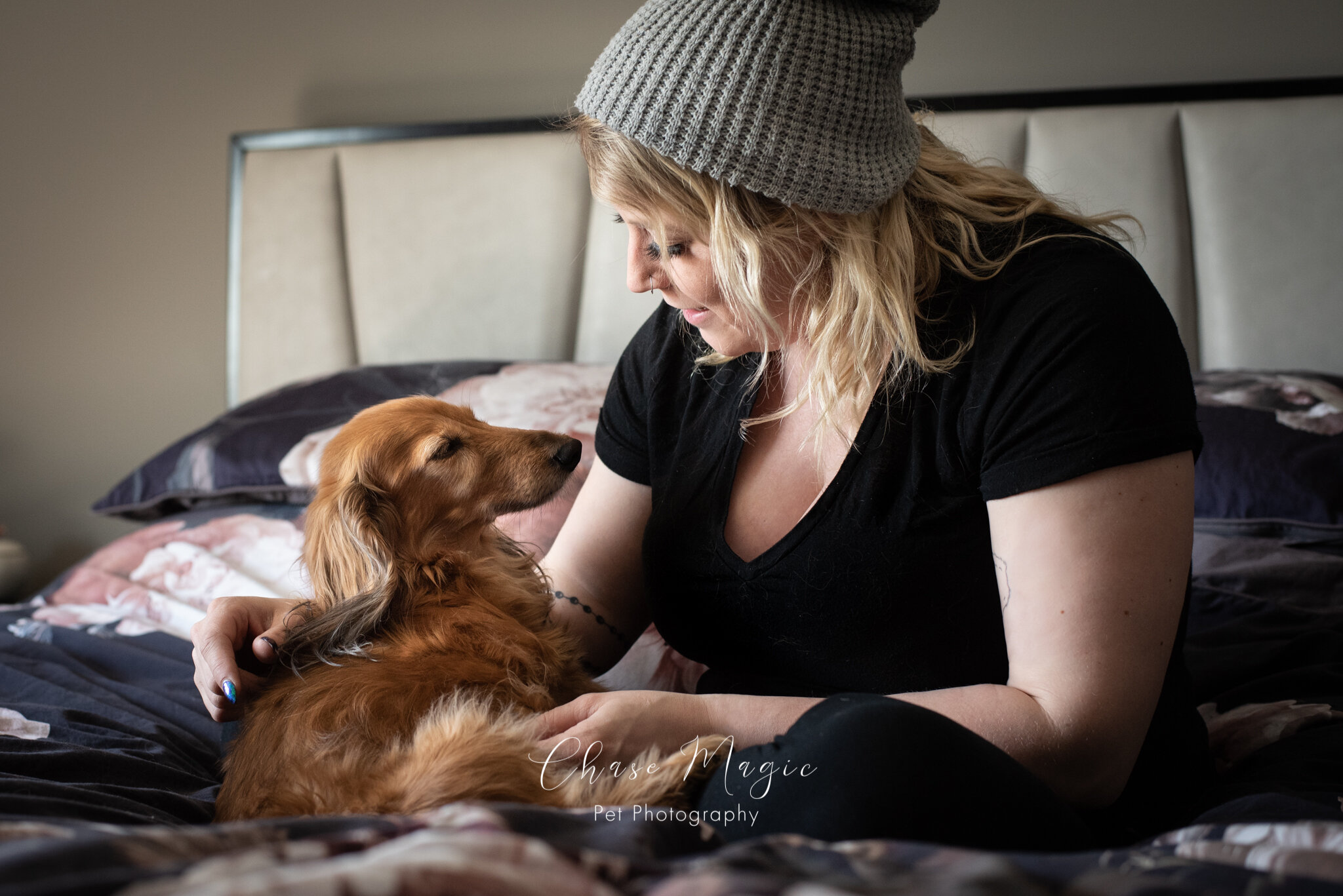 A small dog on the bed with a women in a hat