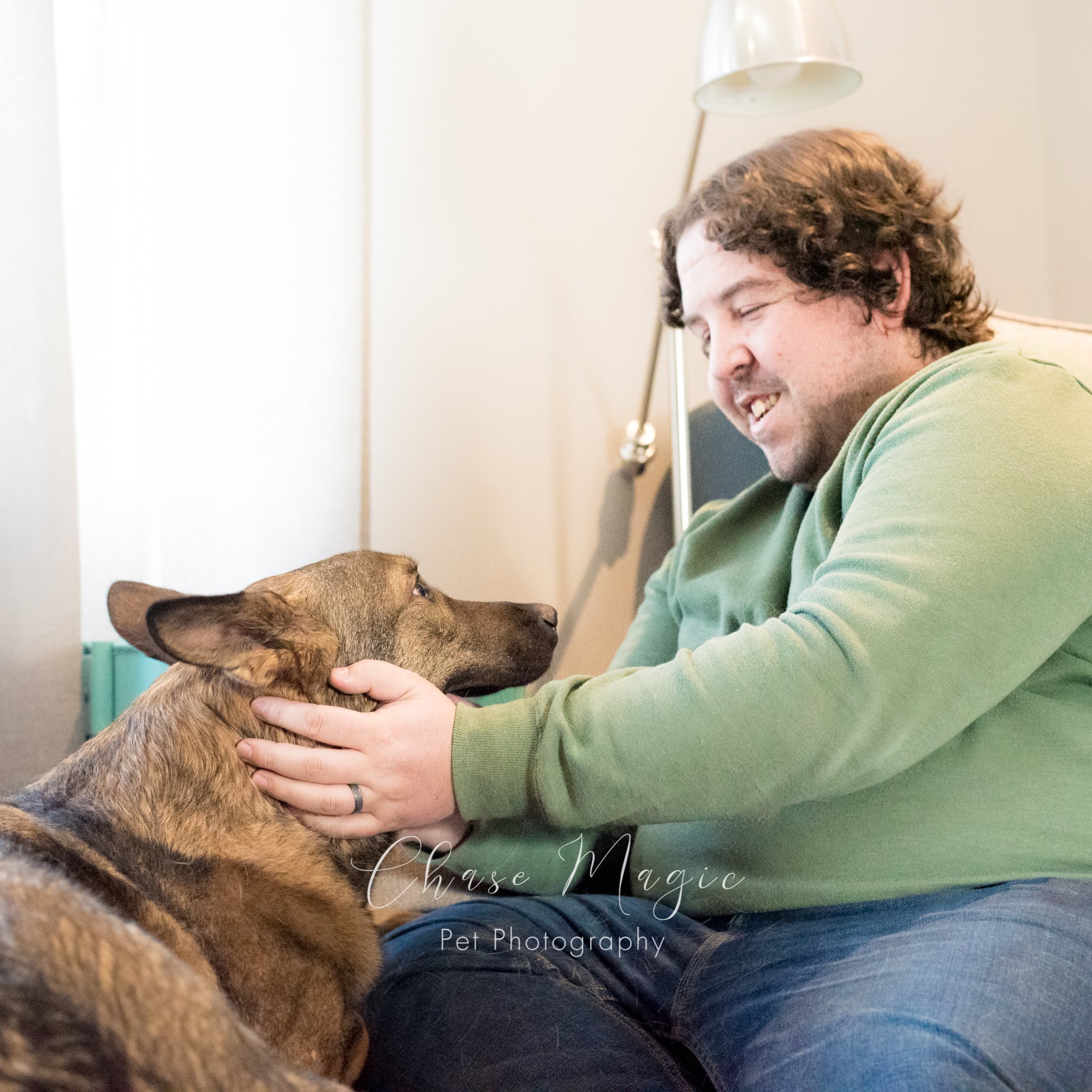 a man in a green shirt petting his german shepard dog