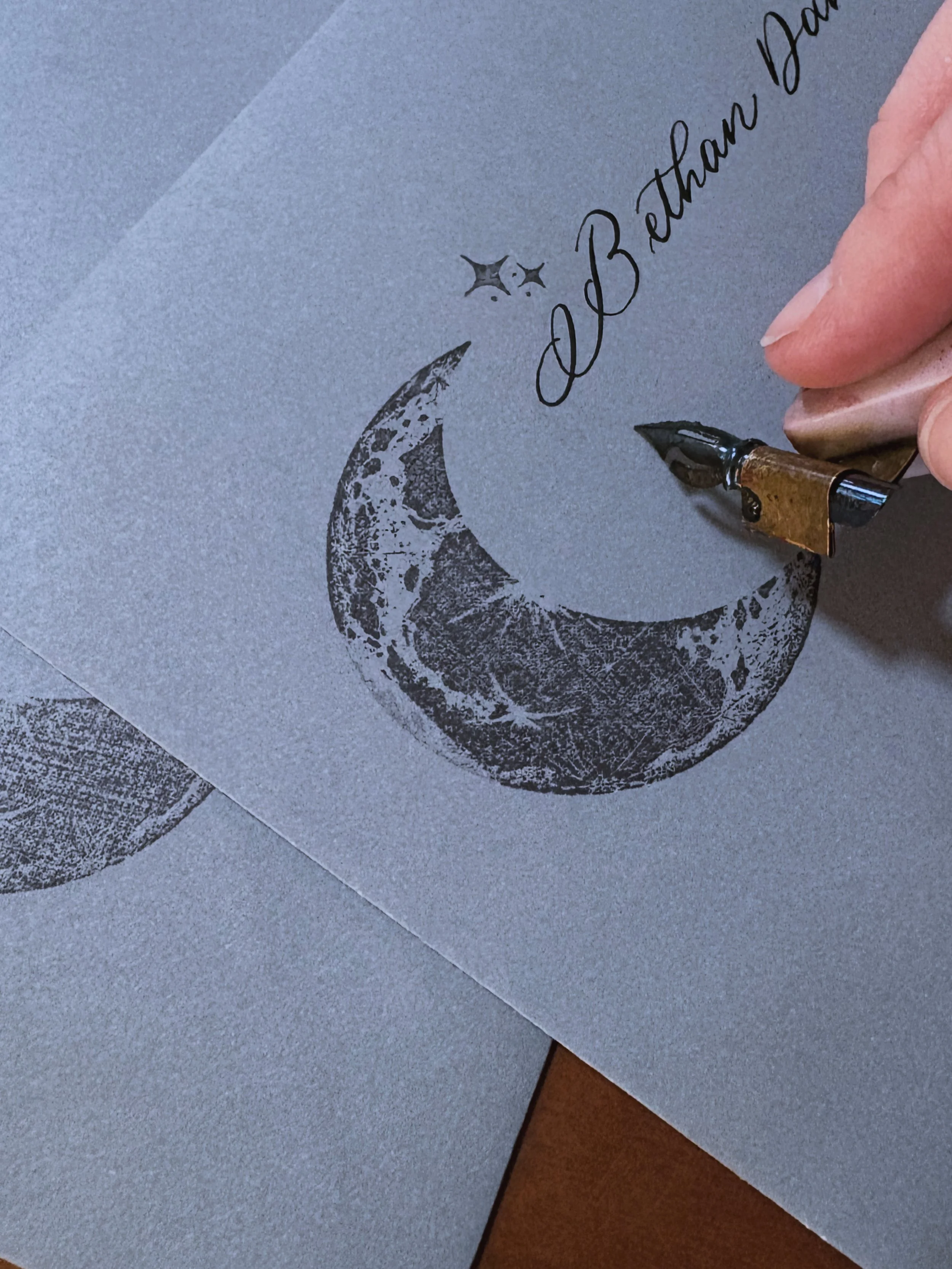 A person's hand is using a fountain pen to write on paper with a crescent moon and stars design, along with the words 'Thank You Dad' in cursive.