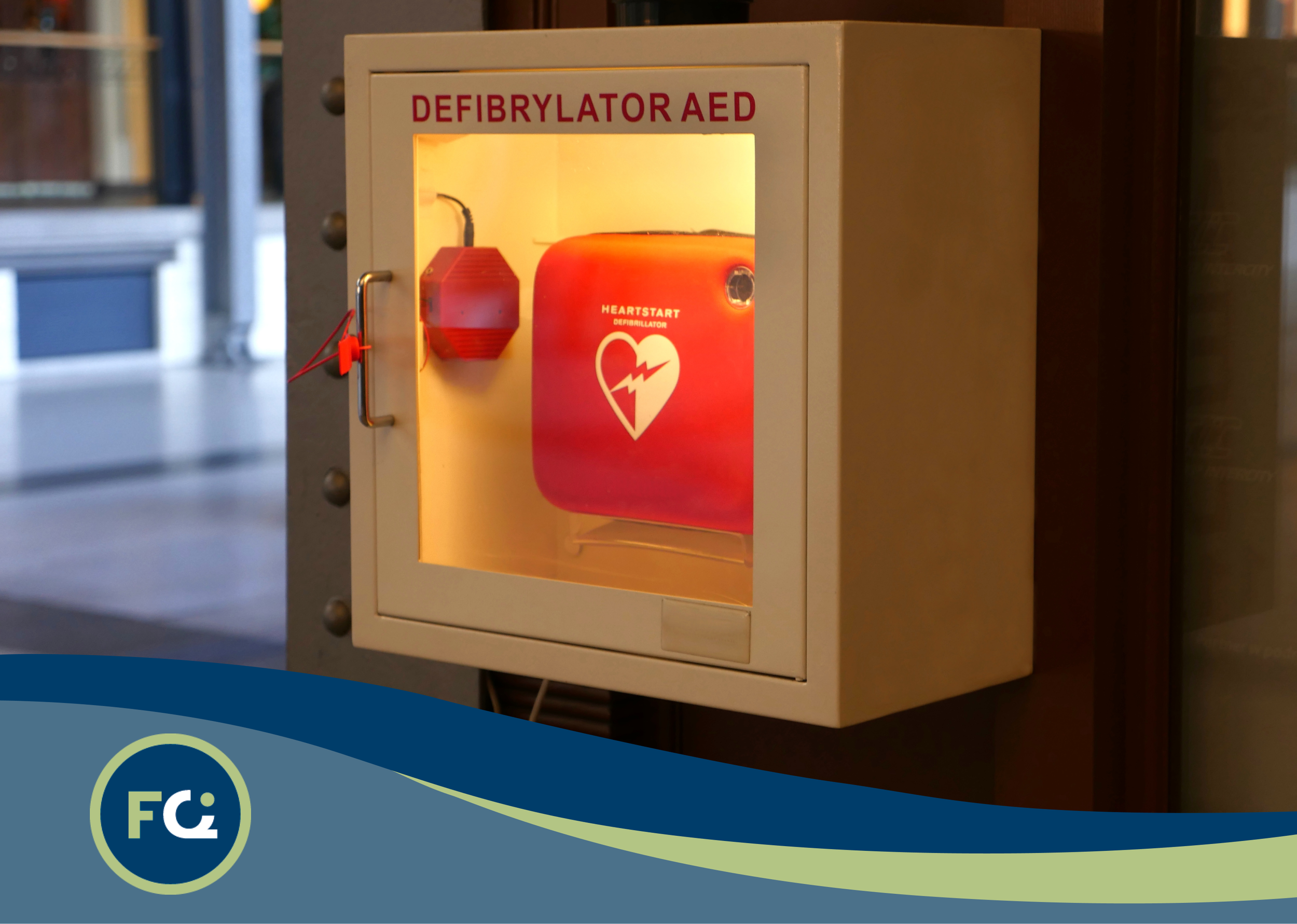 A red automated external defibrillator (AED) inside a protective box mounted on a wall, with the text 'DEFIBRATOR AED' above it.