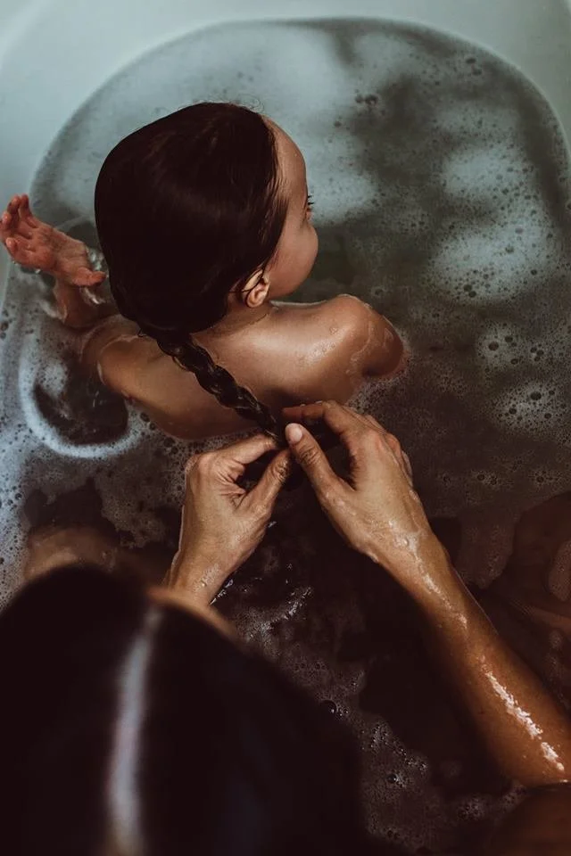 Mother braids daughter's hair in South Florida bathtub.