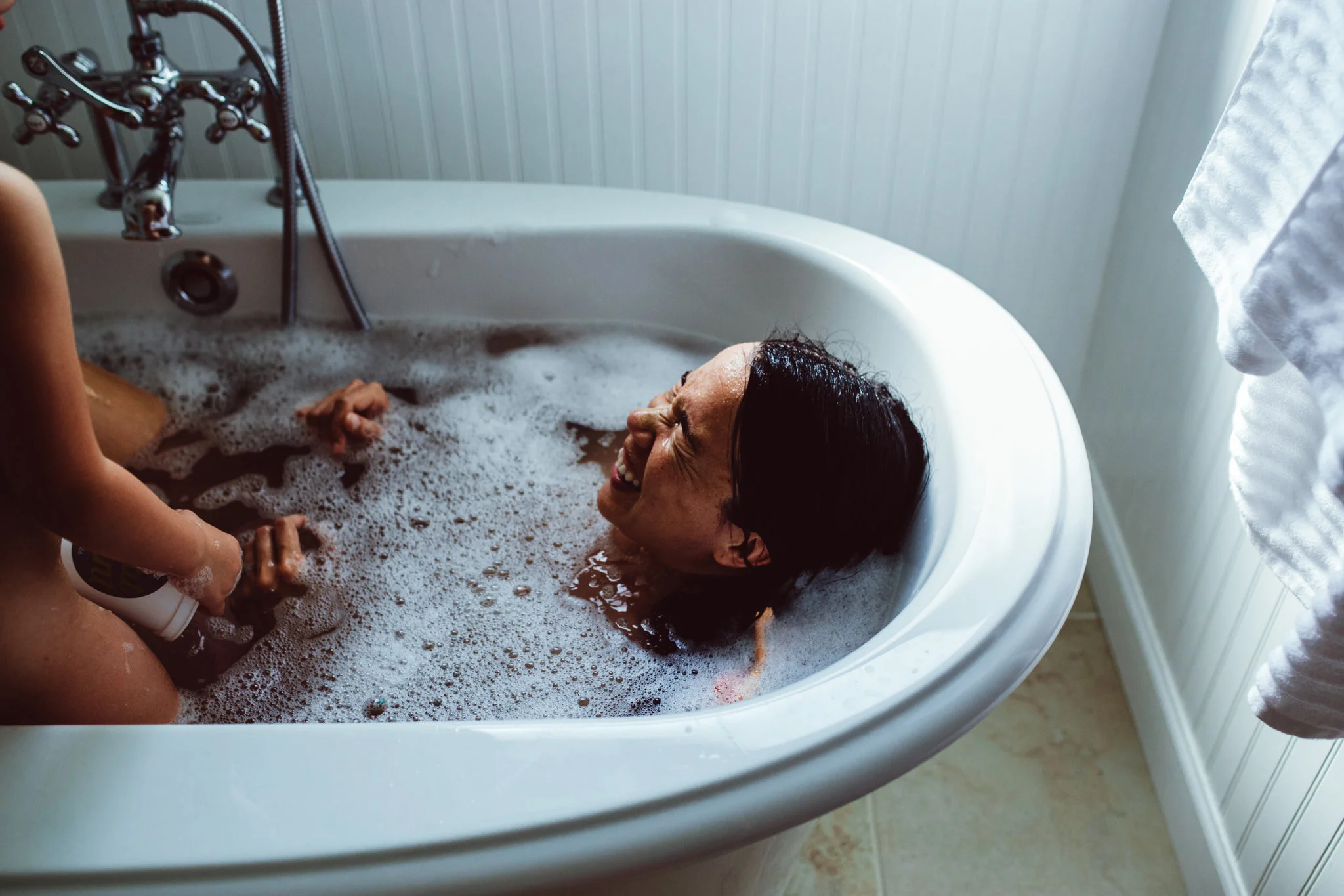 Mother laughs at daughter in bathtub during family documentary photo session