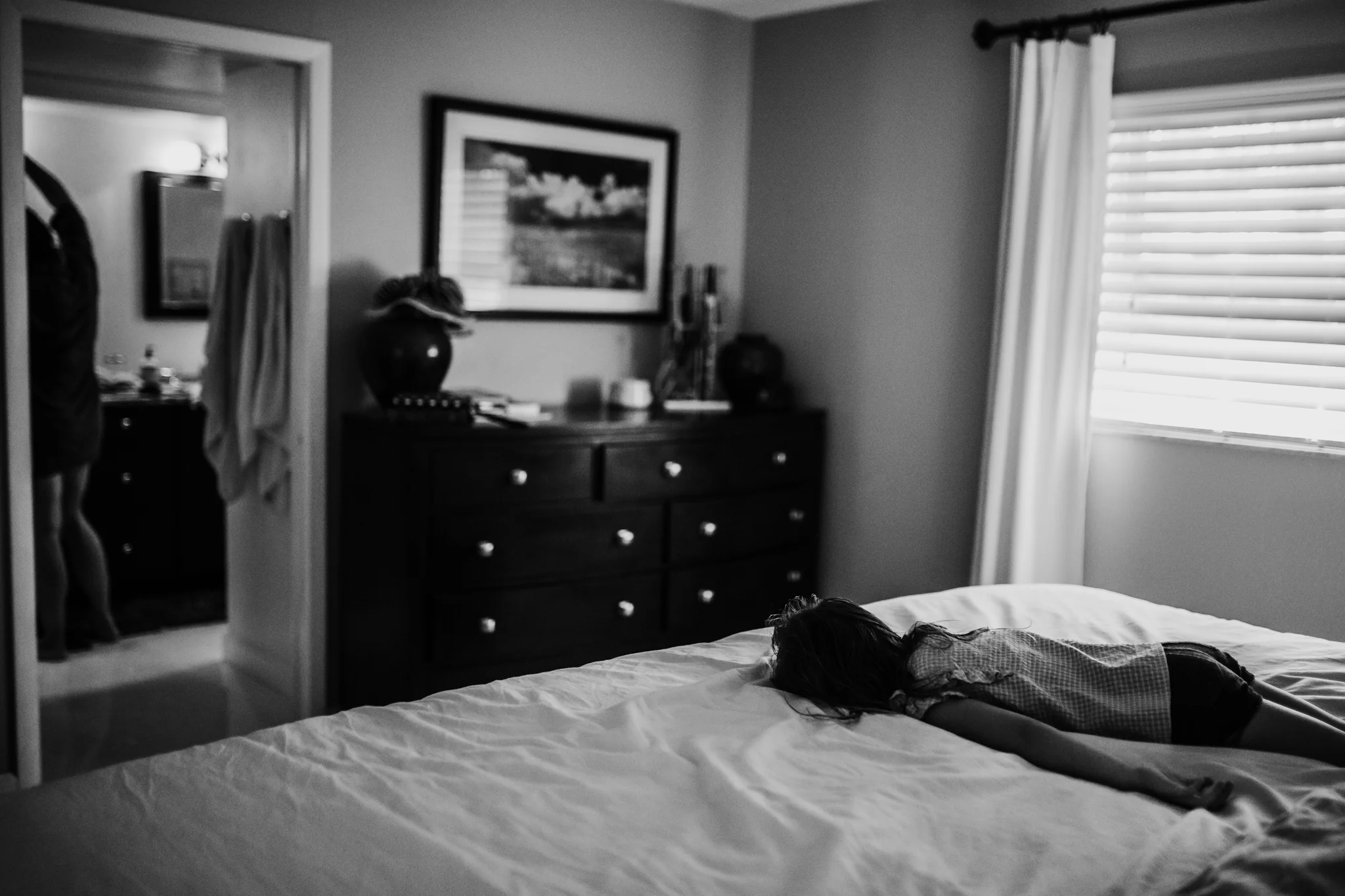 Little girl lays face down on bed while mom blow dries hair
