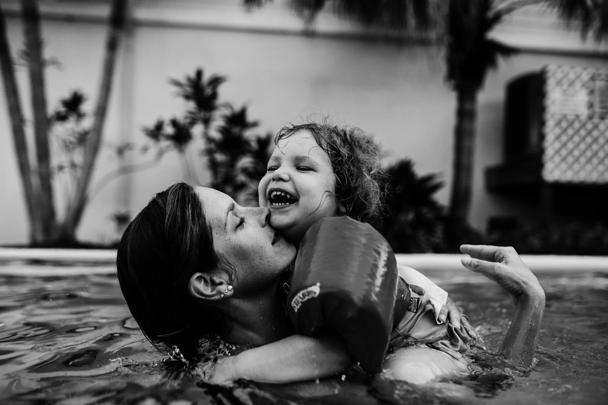 Mother holds daughter in pool while the little girl laughs 