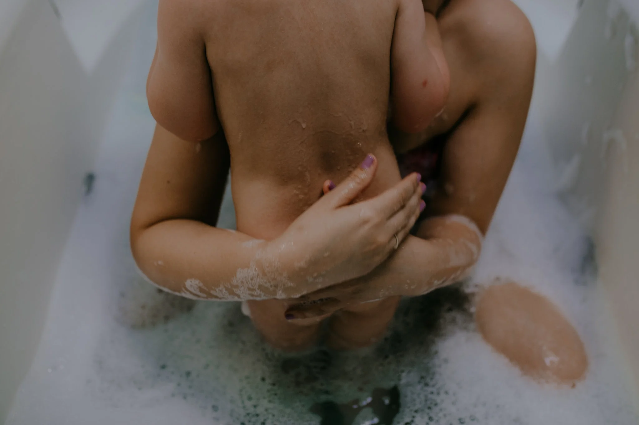 Mother holds toddler close in bathtub