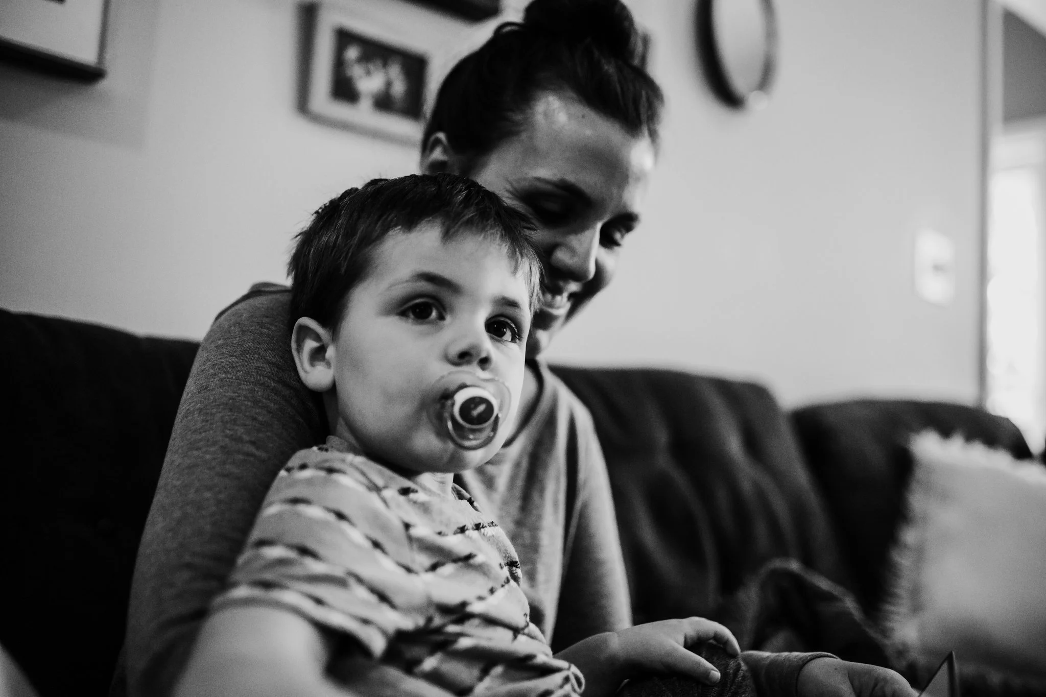 Mother and son sit on couch together as son looks at TV and mom laughs
