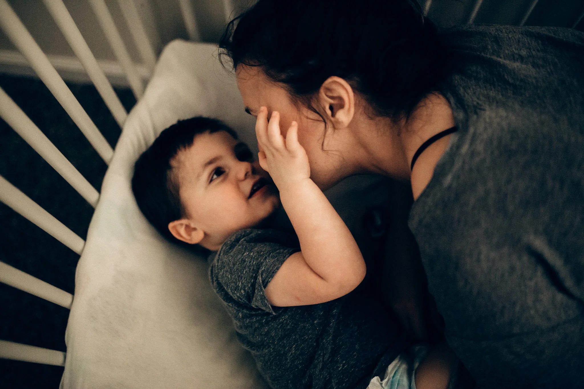 Little boy touches mom's face in his crib