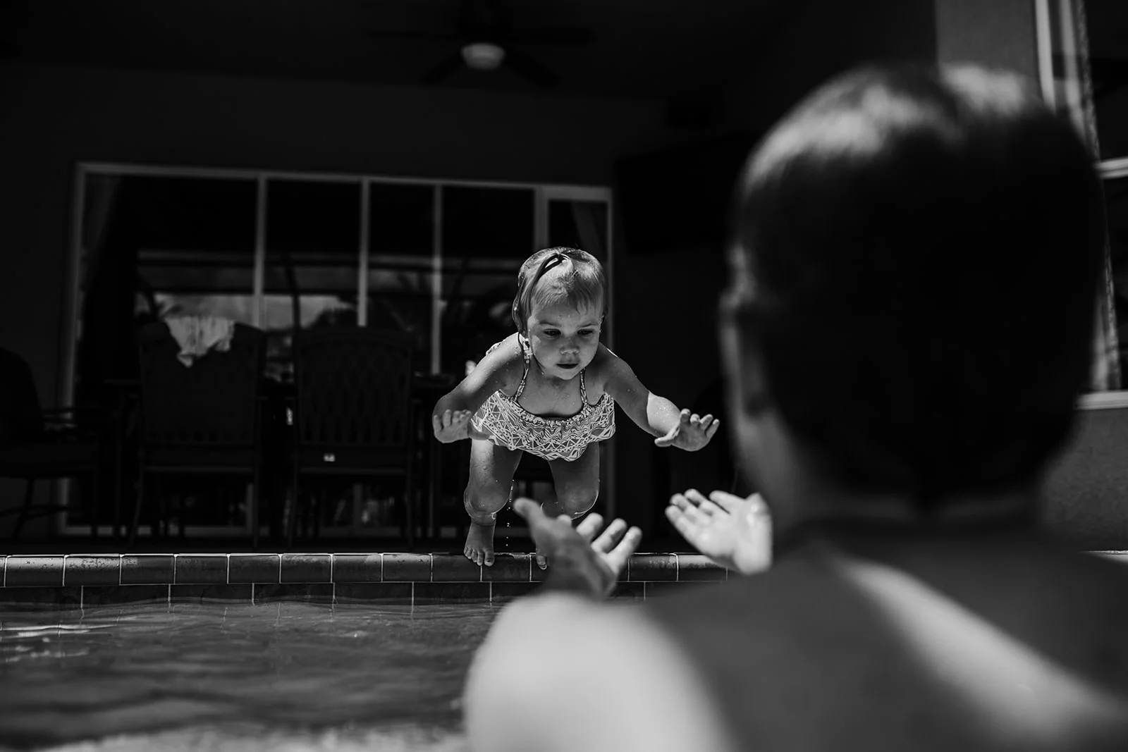 Little girl jumps in the pool towards dad
