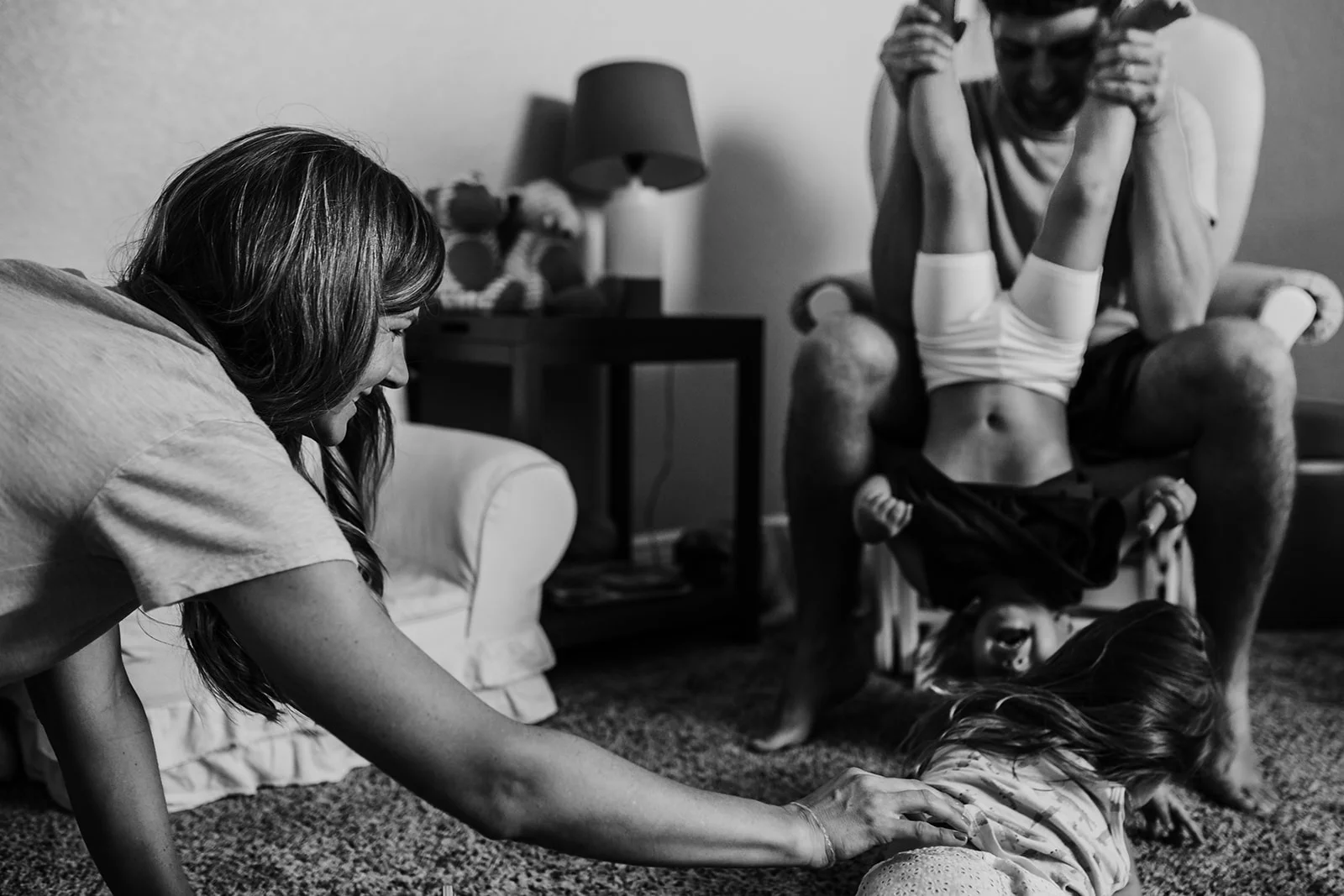 Family goofing around at home as dad holds toddler upside down