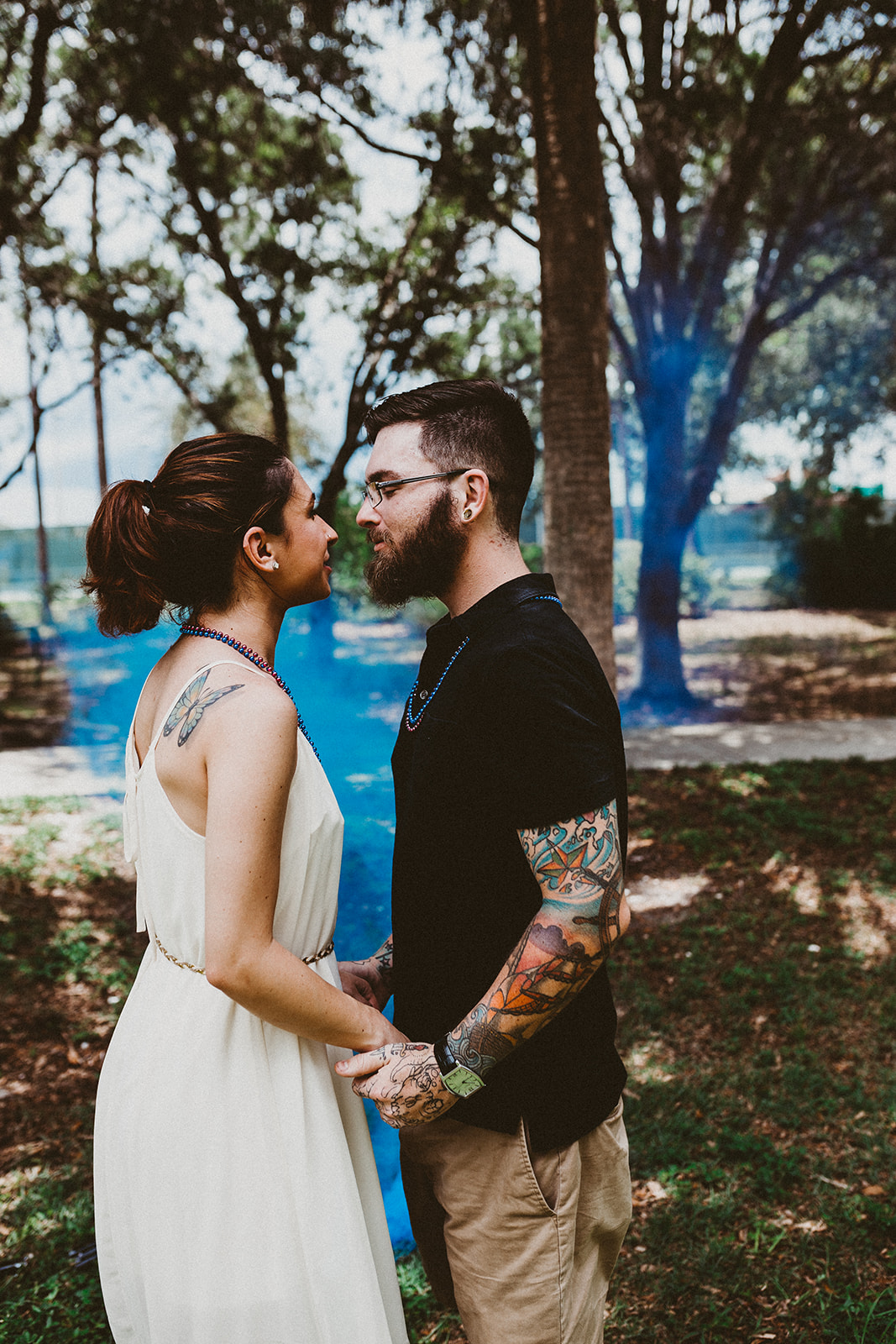  Couple embraces in front of blue smoke during baby gender reveal at Three Oaks Park Fort Myers  