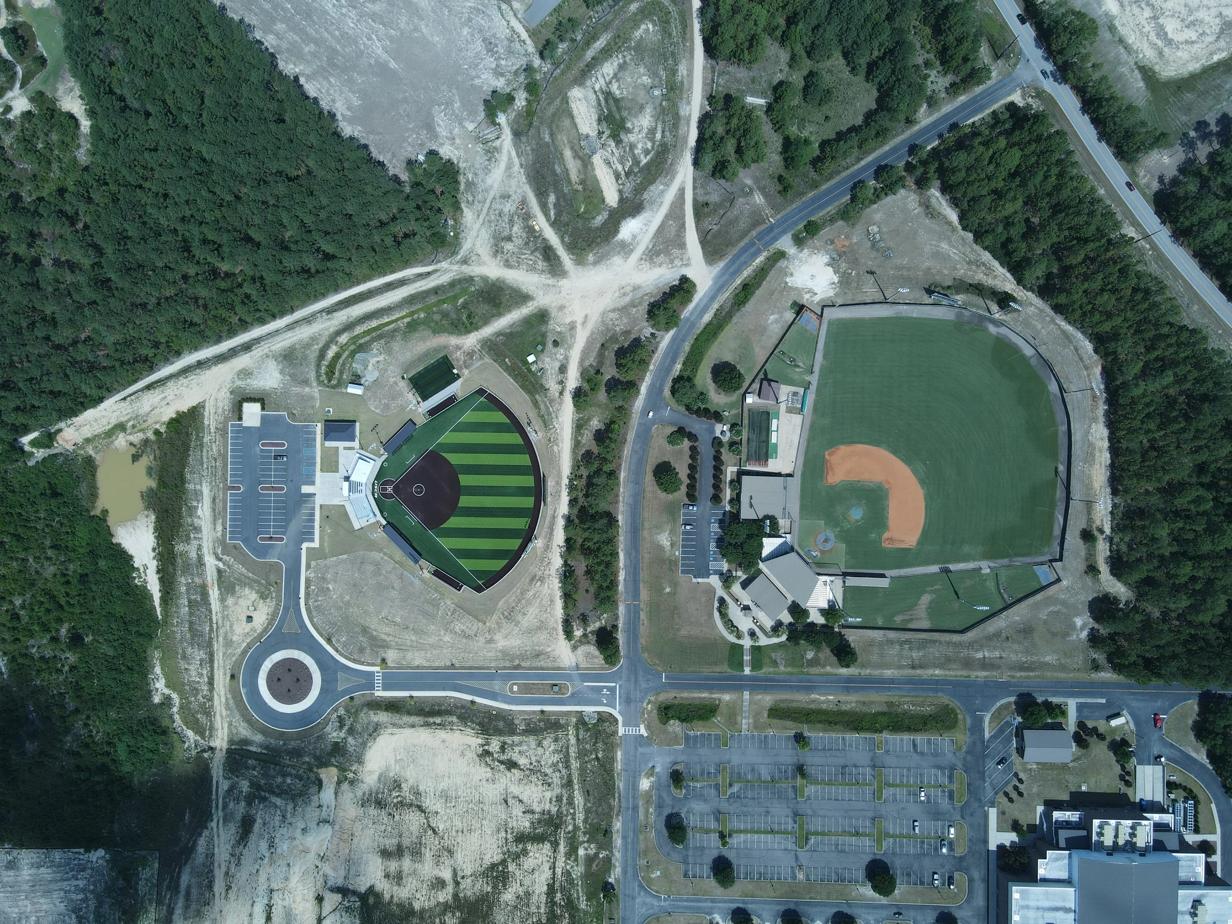 An aerial view of a sports complex showing two baseball fields, a parking lot, and surrounding trees.