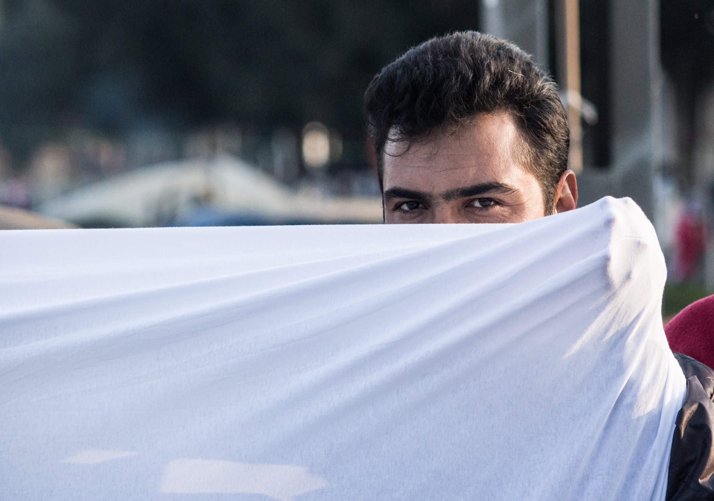 A man peers over a sheet used to make a banner during a peaceful protest in Idomeni, March 2016.