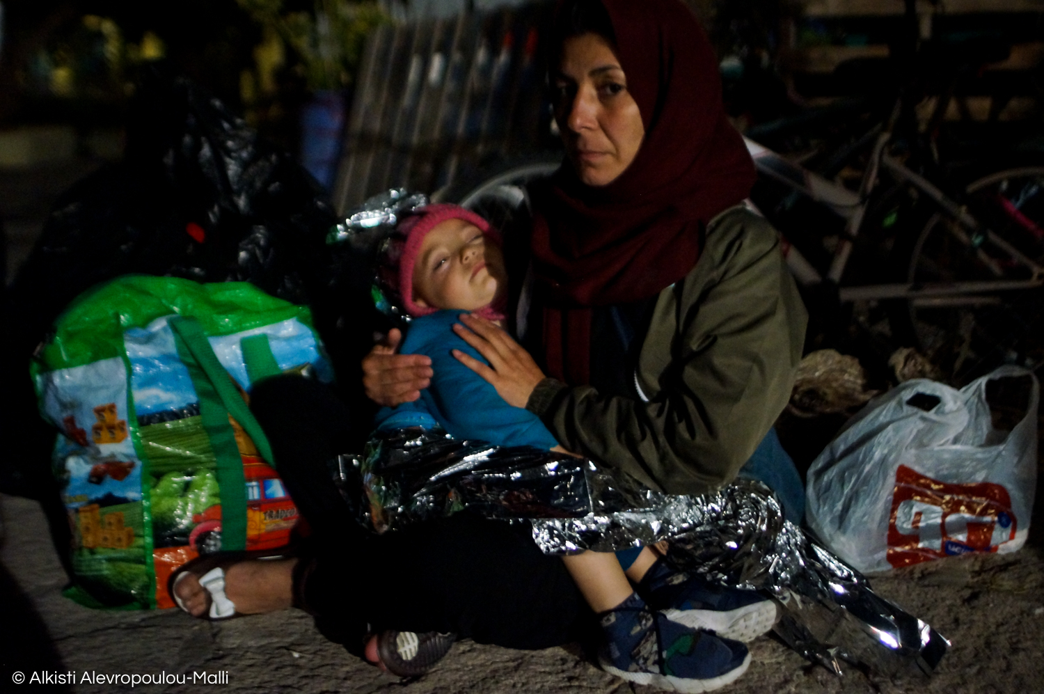 A woman comforts her child, wrapped in an emergency blanket, during a late-night disembarkation in the port of Skala Sikamineas.