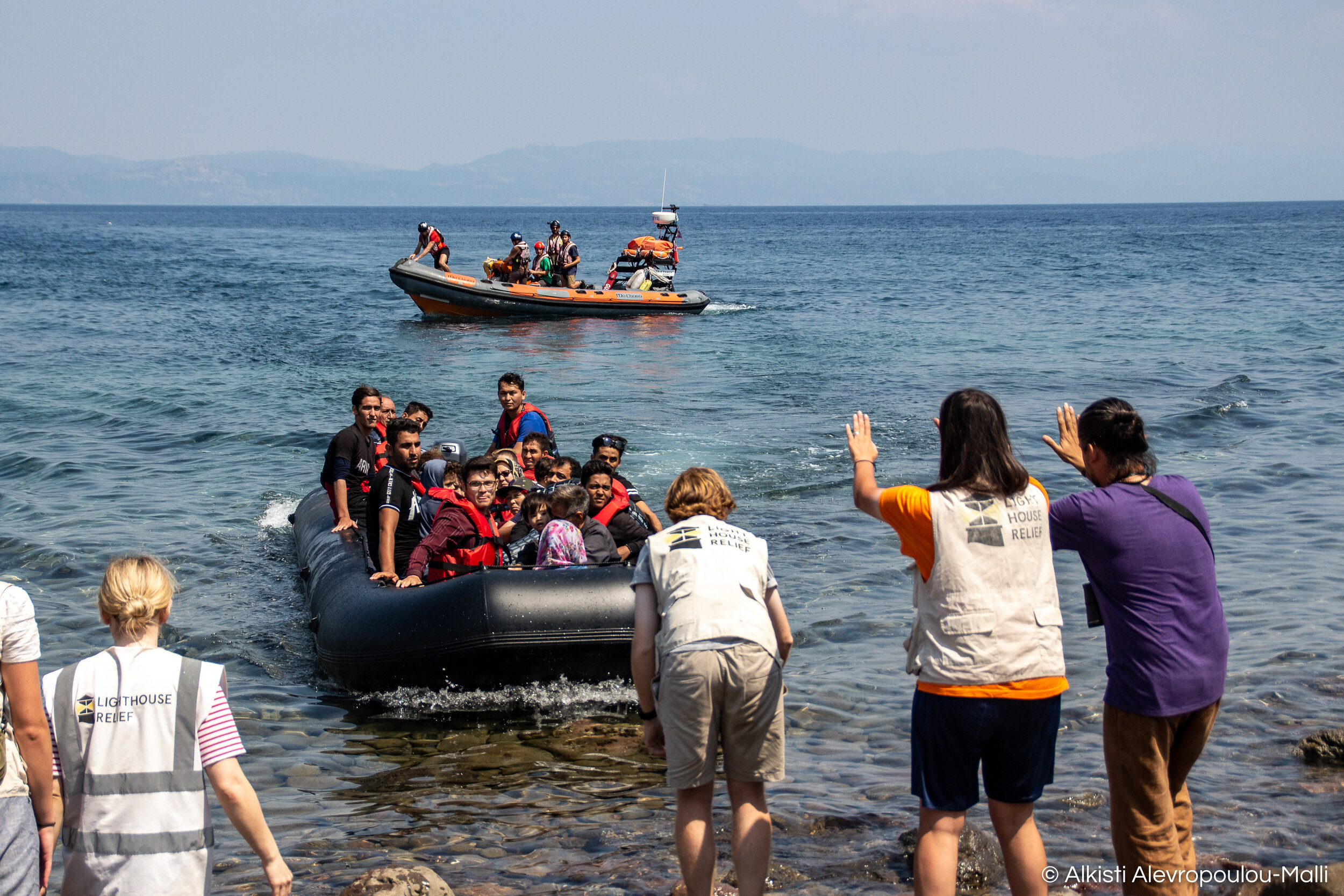 A specially trained team of volunteers receive a dinghy full of people and motion for the boat to slow down as it approaches the beach.