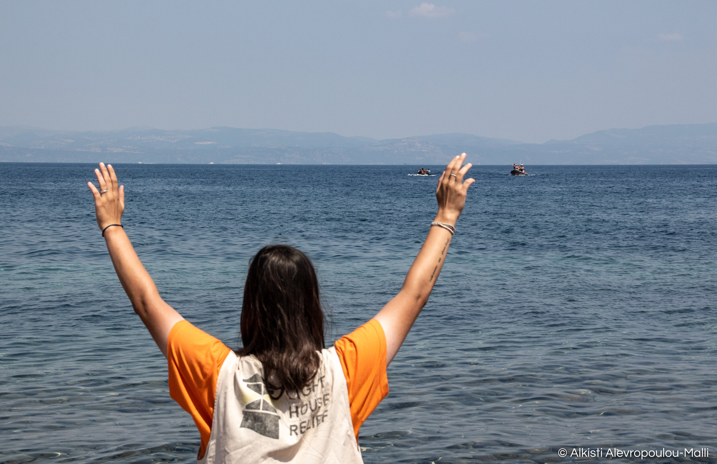 The Emergency Response Officer of humanitarian relief organisation Lighthouse Relief signals to an approaching migrant dingy that is being escorted safely to shore by the Search and Rescue boat.