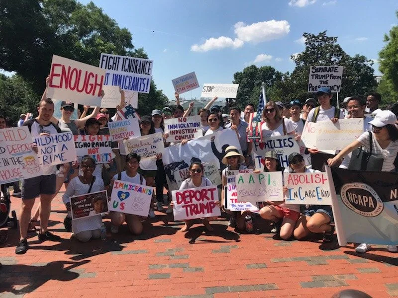 A large group of advocates pose for a group photo. They are all holding signs in support of immigrants and keeping families together.