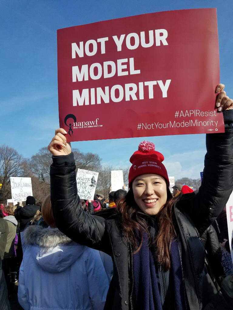 An AAPI Woman holds a “not your model minority” sign high at a rally.