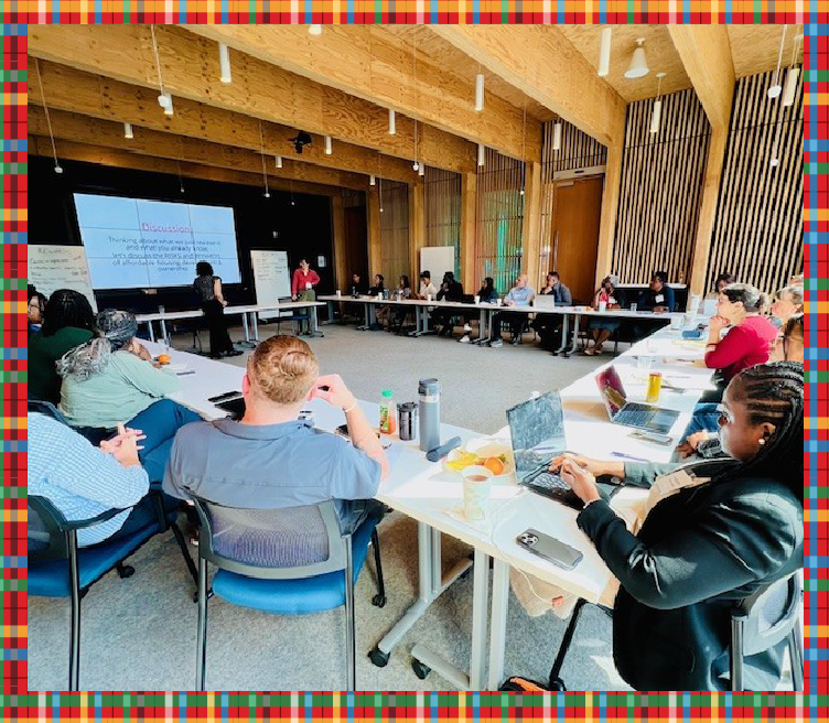 Photograph of a large room with about 30 people sitting at long tables arranged in a U-shape, watching a presentation by HDC staff.