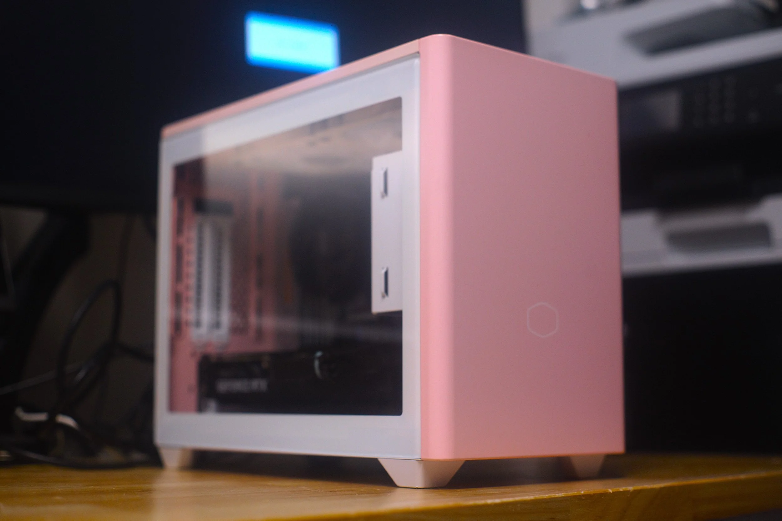 Small pink and white computer case with a transparent side panel, placed on a wooden surface.
