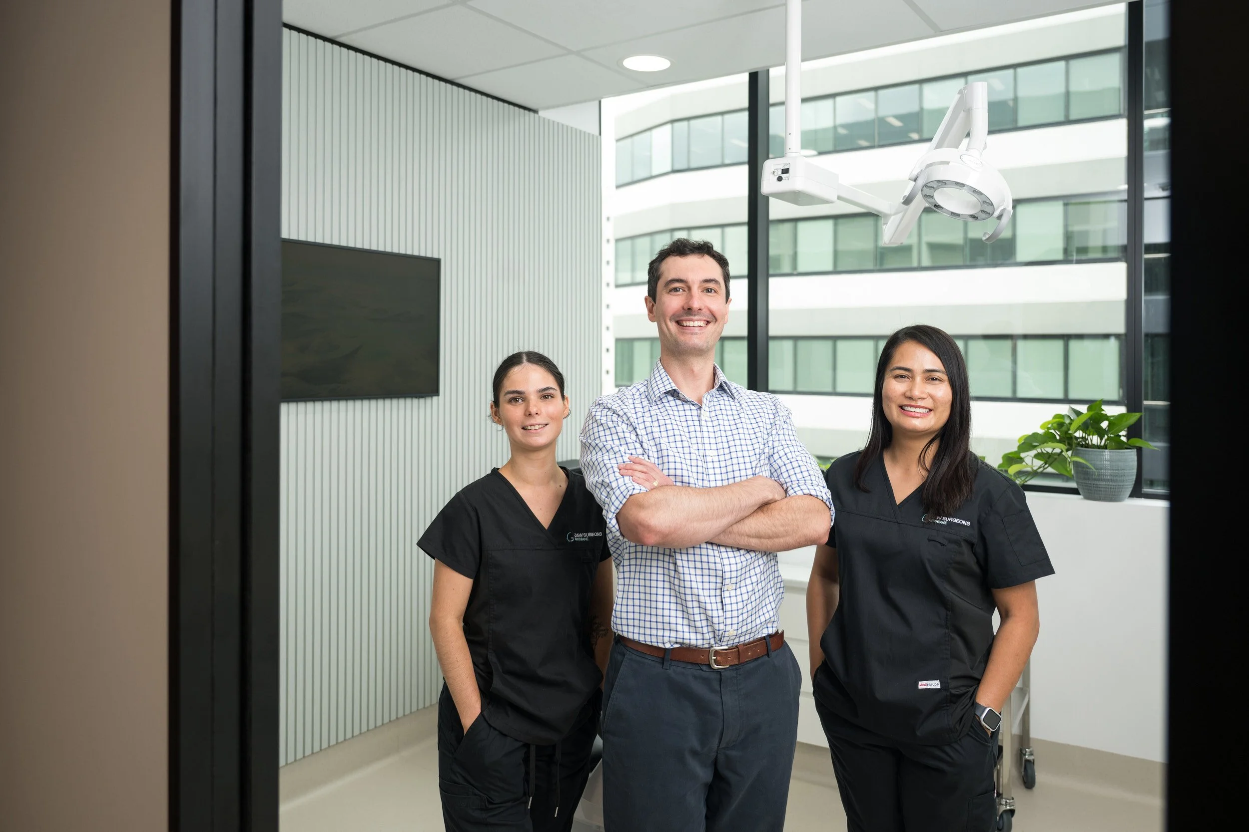 Team corporate photography of three medical professionals, two women and one man, standing together inside a modern medical facility, smiling at the camera.