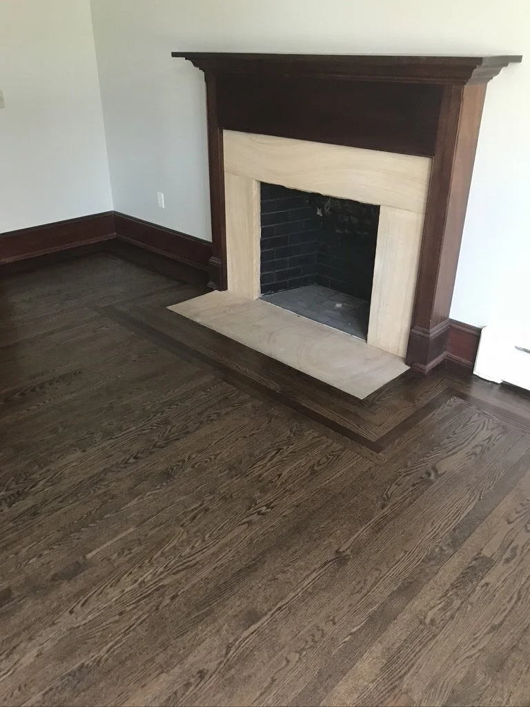 The same living room floor after refinishing with a dark stain, border framing the fireplace, Fairfield, CT