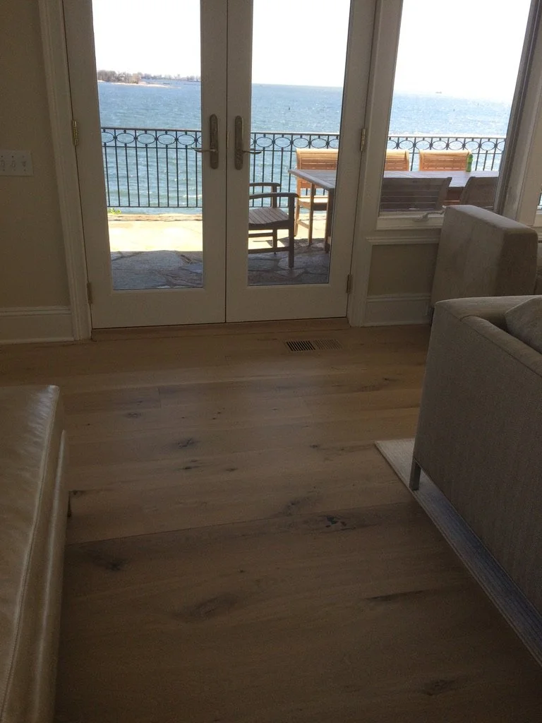 Floor sander mid-pass on a hardwood installation in a Stamford, CT home, with French doors opening to a water view