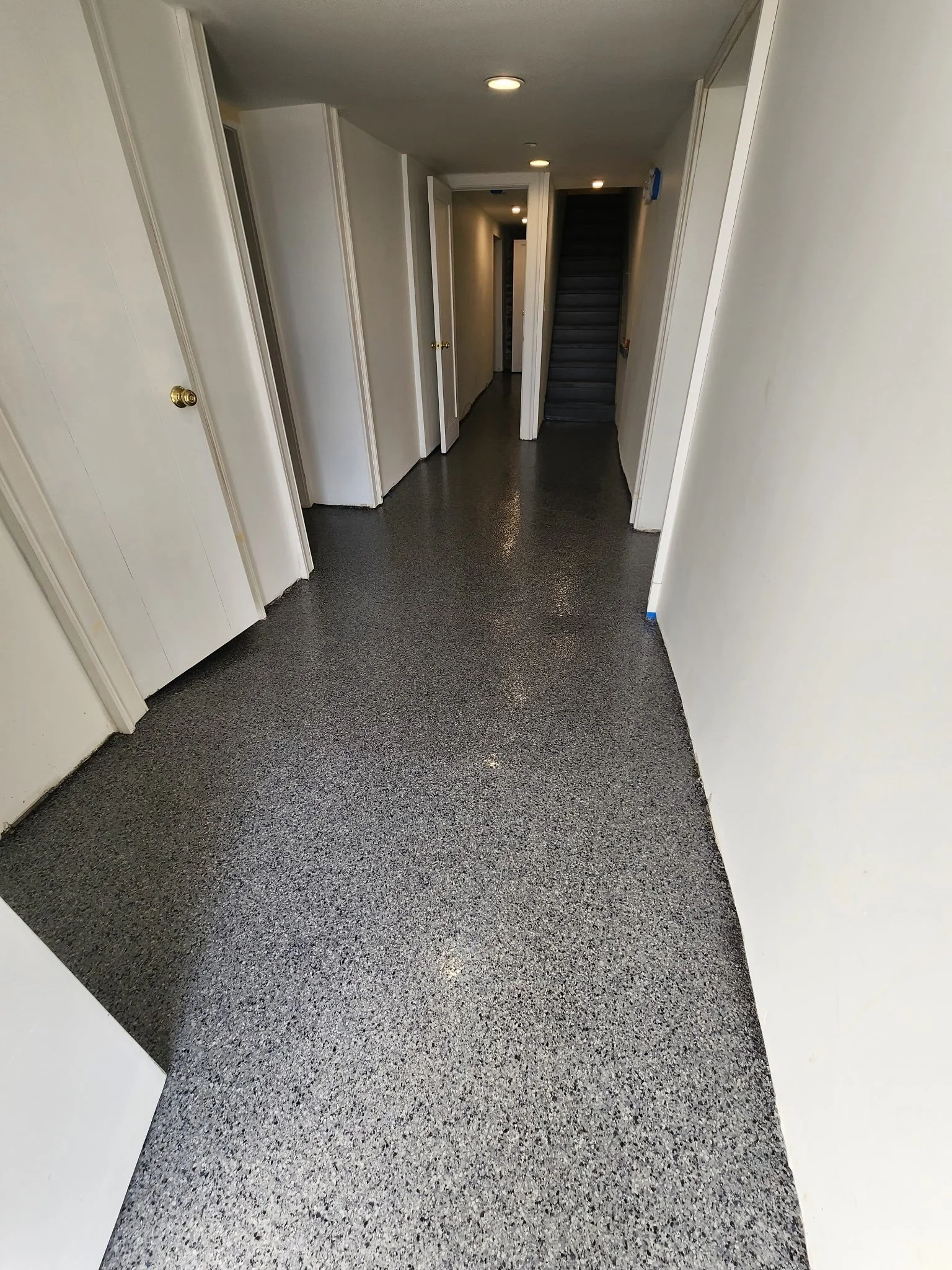 Finished flake epoxy basement corridor leading toward an exposed stone foundation wall, Danbury, CT