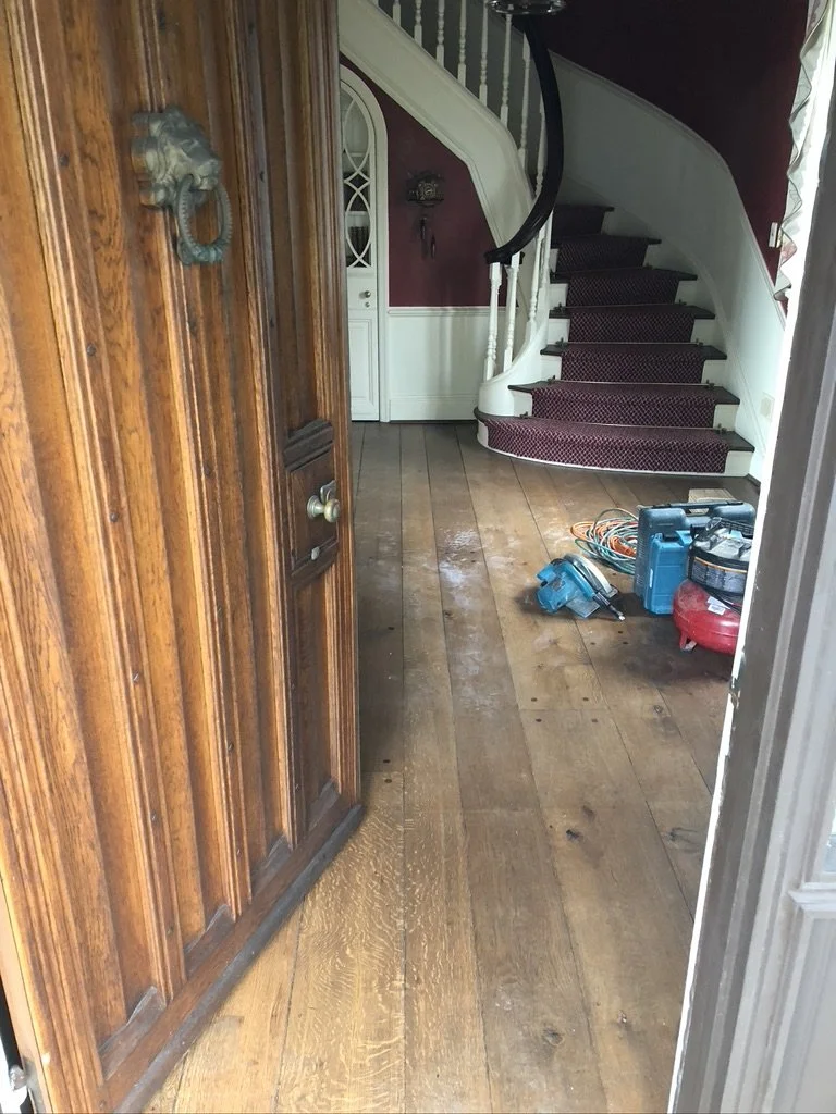 Worn, dull oak floor in a foyer with a curved staircase before refinishing, Stamford, CT