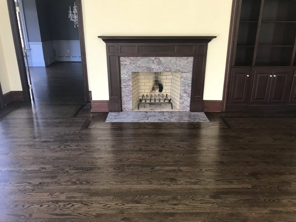 The same living room floor after refinishing with a dark stain, border framing the fireplace, Fairfield, CT