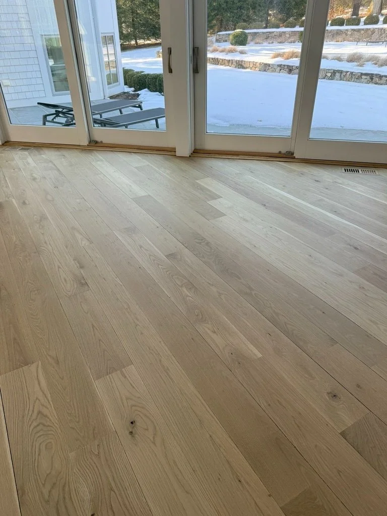 Overhead view of an octagonal turret-style landing and staircase finished in wide-plank white oak, snow visible through the windows, Danbury, CT