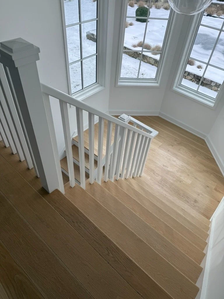 Overhead view down a wide-plank white oak staircase leading to a sunlit hallway in a Danbury, CT home