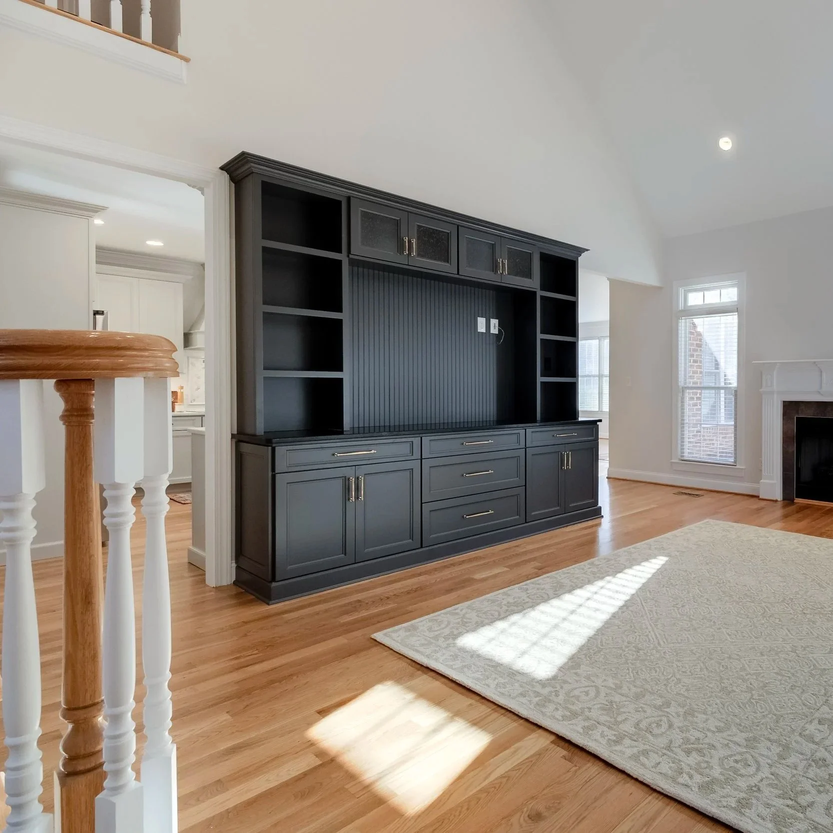 Living room with a large black built-in entertainment center, hardwood floors, a beige area rug, and windows letting in natural light.