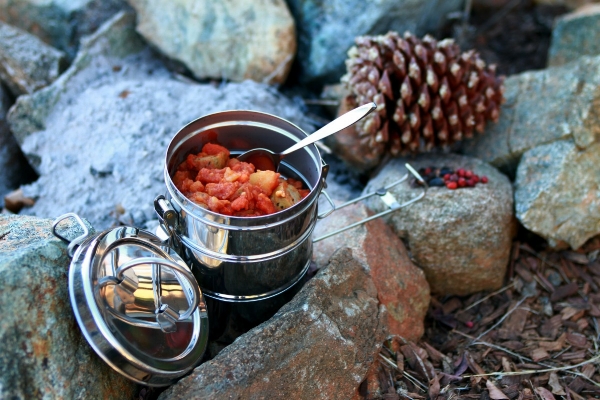 Steel cooking pot with food inside sitting on rocks outdoors