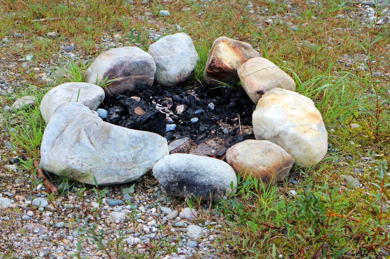 A stone fire ring in a field of grass with charred ground inside the fire ring.