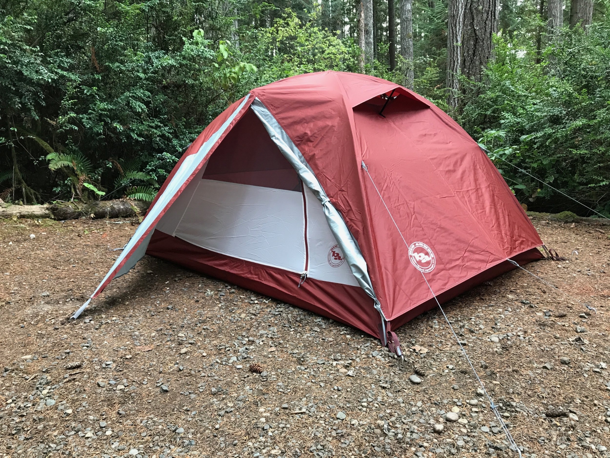 Outdoor dirt campsite with an orange tent surrounded by trees.