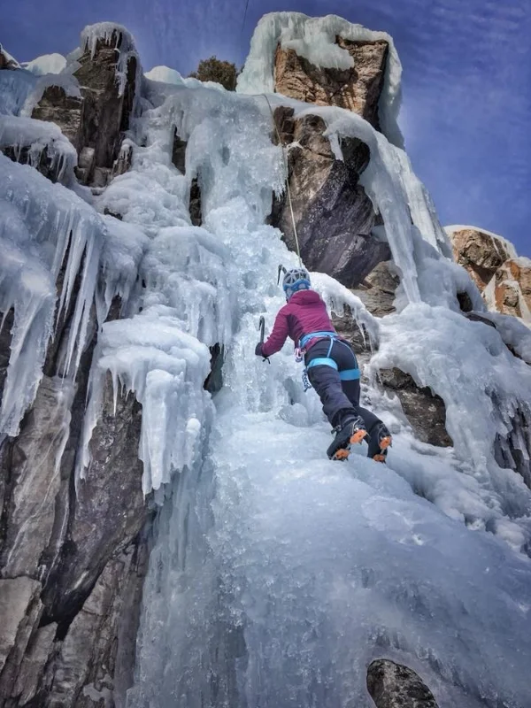A woman in a pink jacket ice climbing.