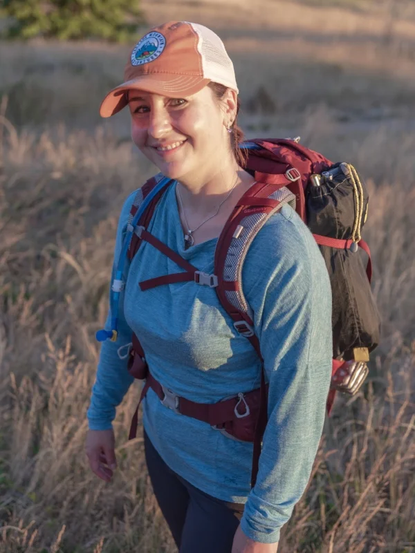 A smiling woman wearing an orange hat and blue shirt standing in a grass field.