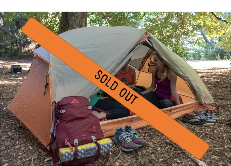 Outdoor dirt campsite with an orange tent surrounded by trees.